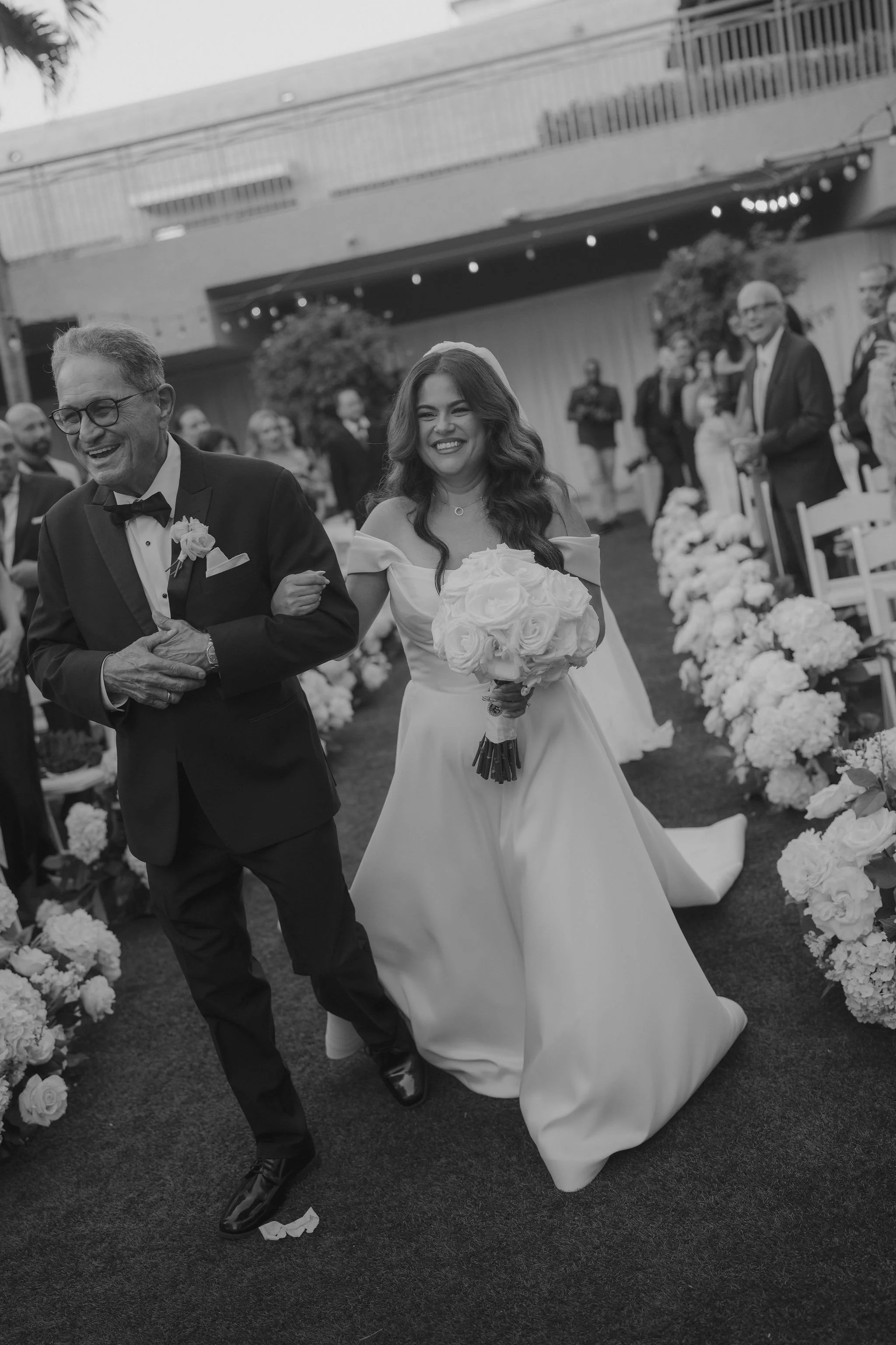 A bride in a wedding dress holding a bouquet walking down the aisle with her father at a wedding ceremony