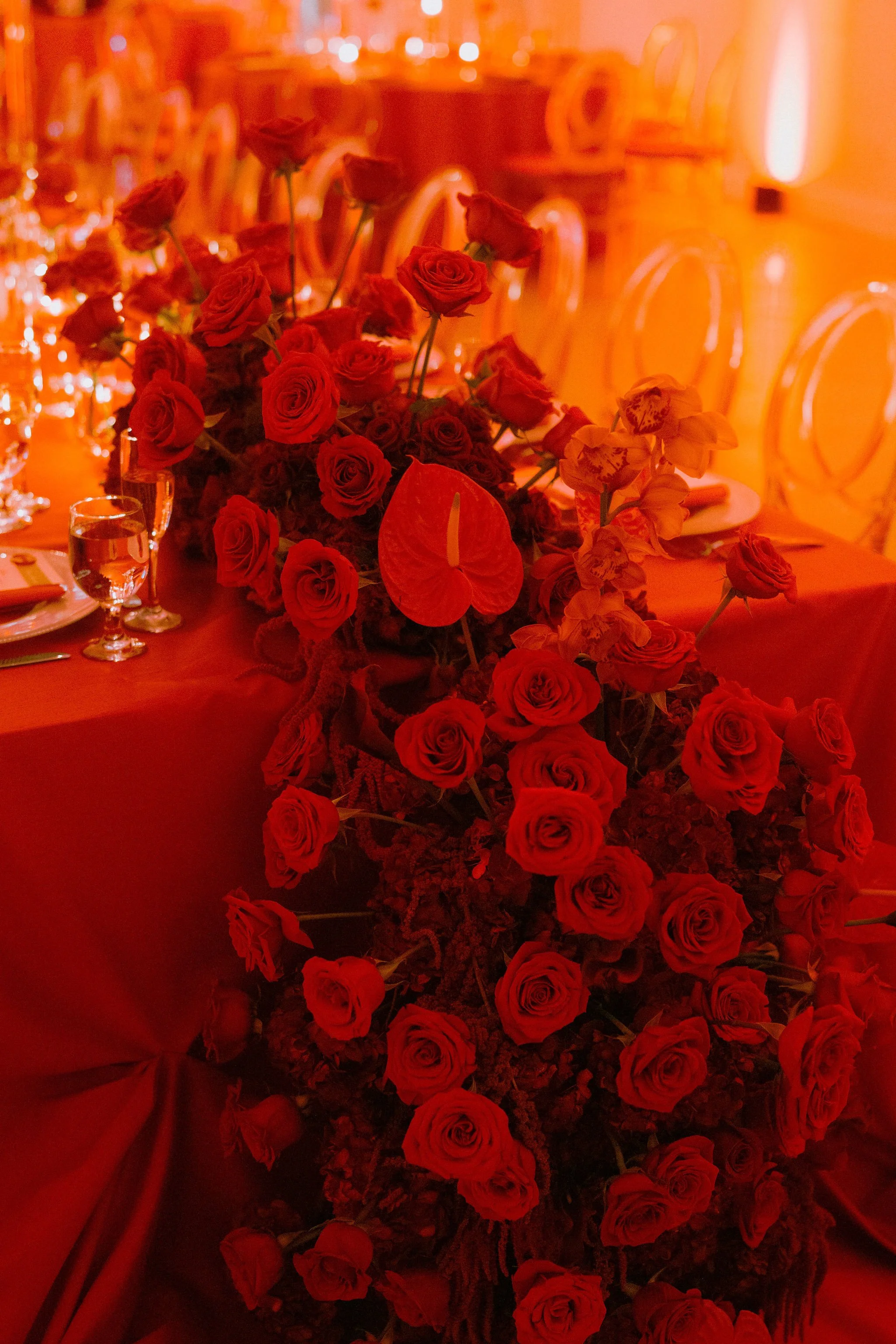 A large floral arrangement of red roses and anthuriums on a banquet table in a warmly lit setting.