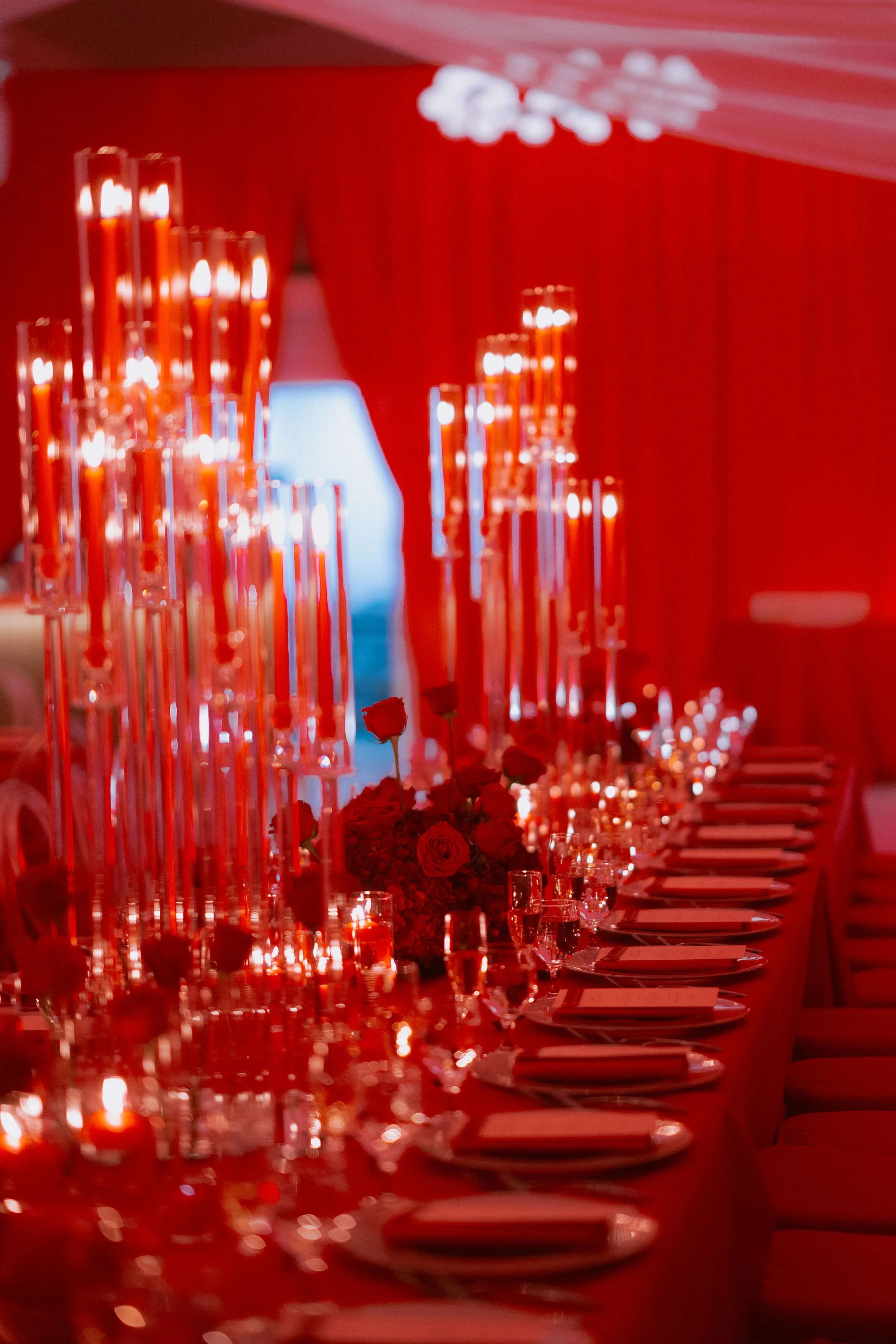 Elegant banquet table decorated with red flowers, tall red candles, and dim lighting with red curtains in the background.
