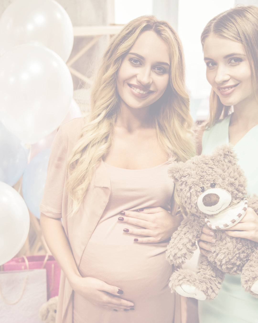 Pregnant woman with long blonde hair smiling, cradling her belly, standing next to another woman with reddish hair holding a teddy bear, in a decorated room with balloons.