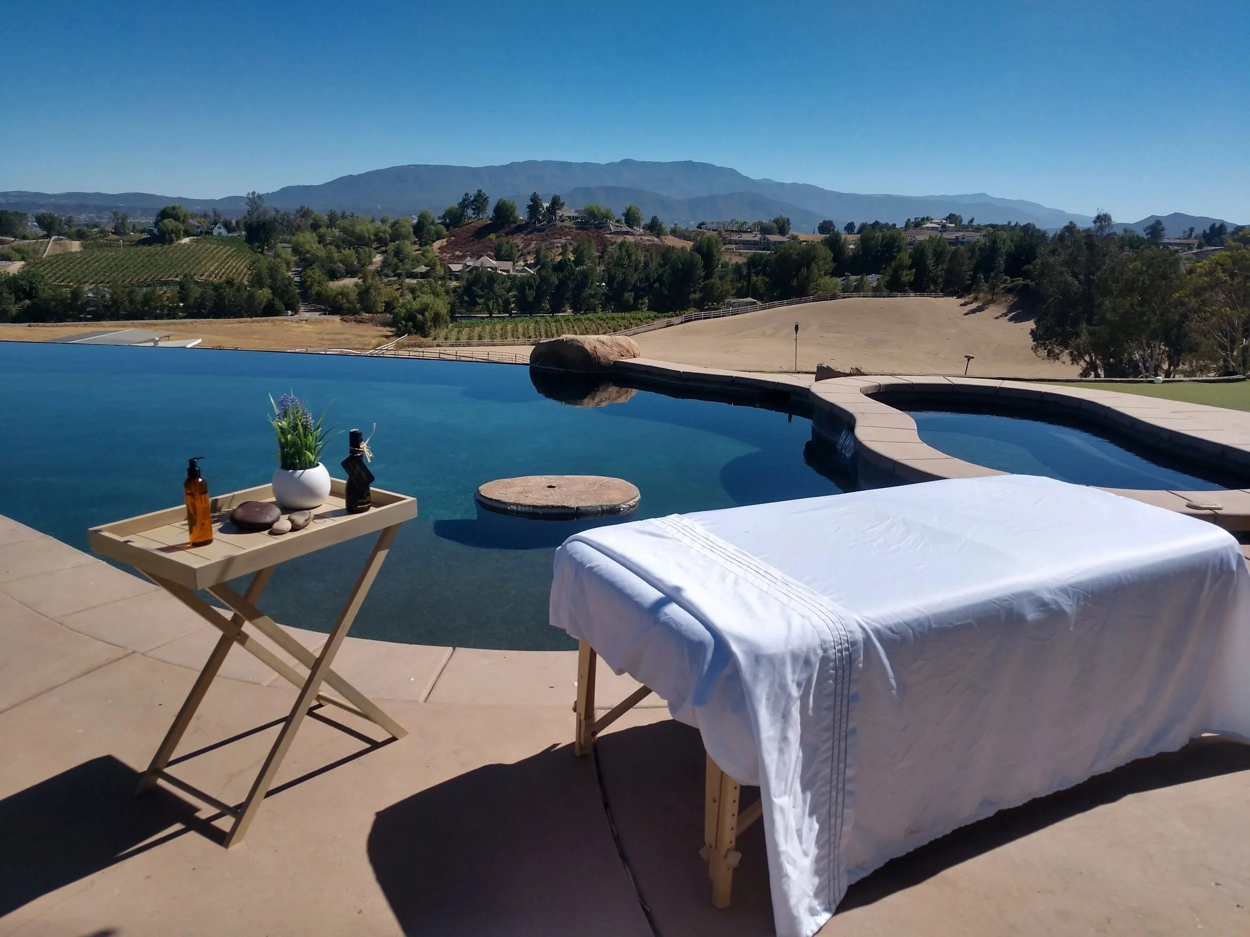 A massage table with white sheets set up by a pool overlooking vineyards for a spa party by Balanced Pro Massage