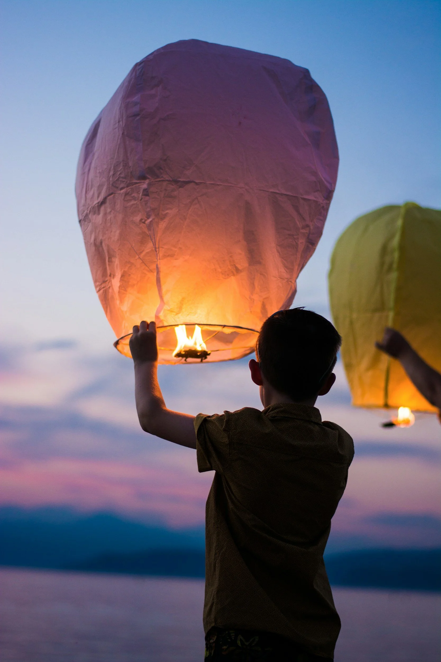 Child releasing a sky lantern at sunset with a clear sky in the background.