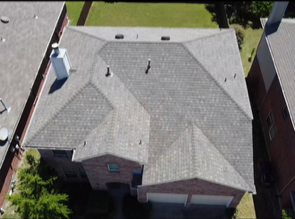 Aerial view of a gray shingle roof on a residential house between neighboring buildings.