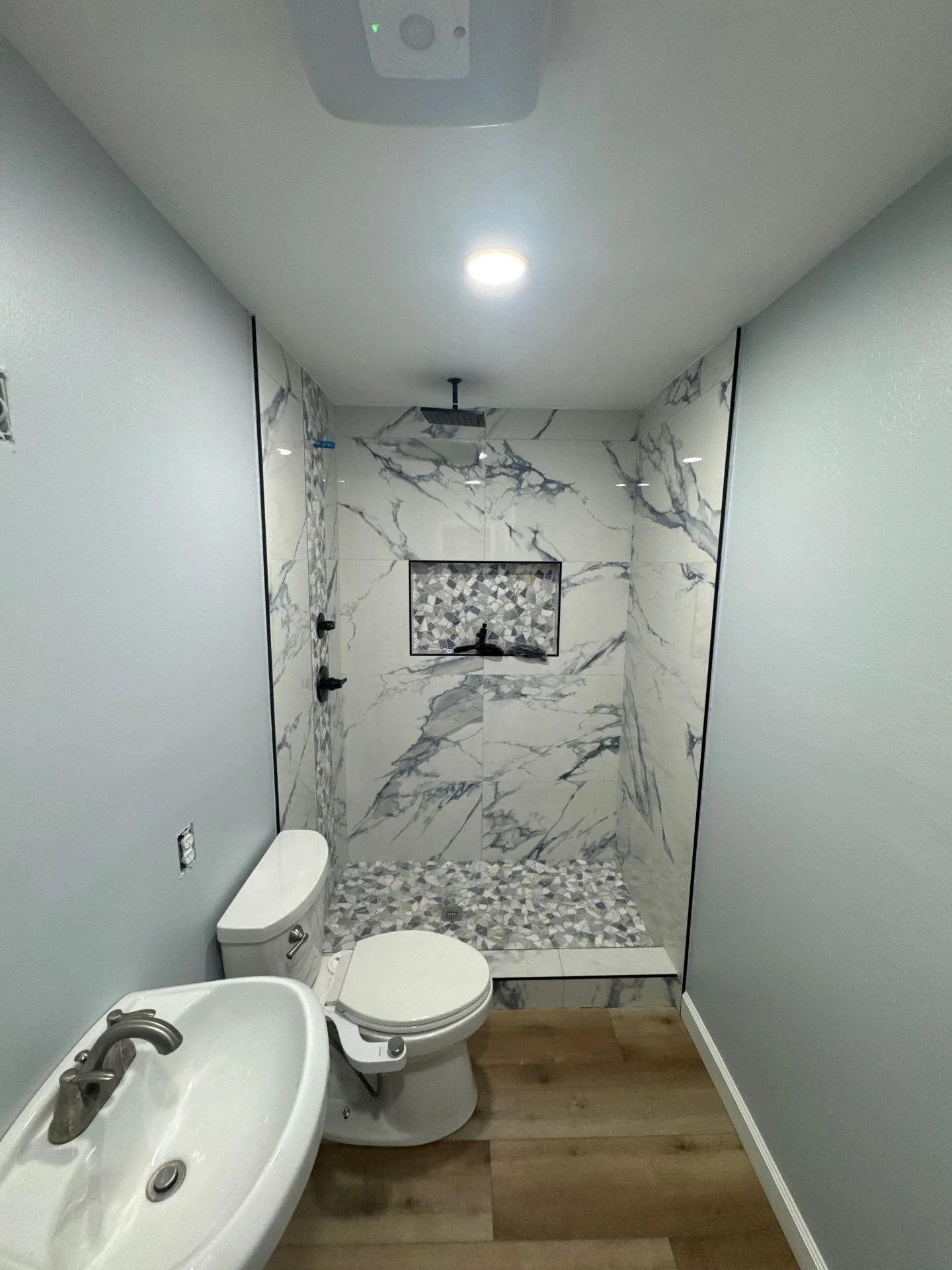Modern bathroom with a marble-tile walk-in shower, mosaic shower floor, white toilet, and pedestal sink.