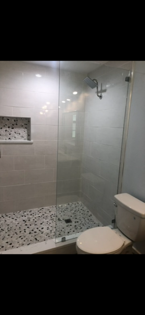 Modern tiled bathroom with glass-enclosed walk-in shower, rainfall showerhead, pebble floor, built-in niche, and white toilet