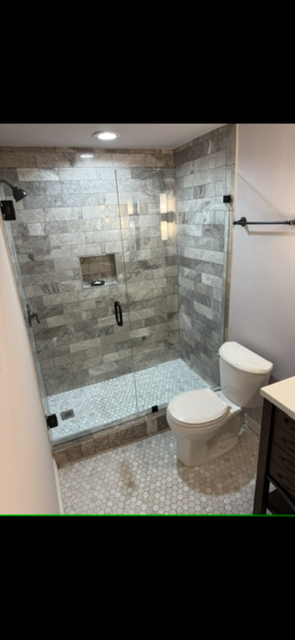 Modern bathroom with a glass-enclosed gray stone tile shower, mosaic floor, and white toilet