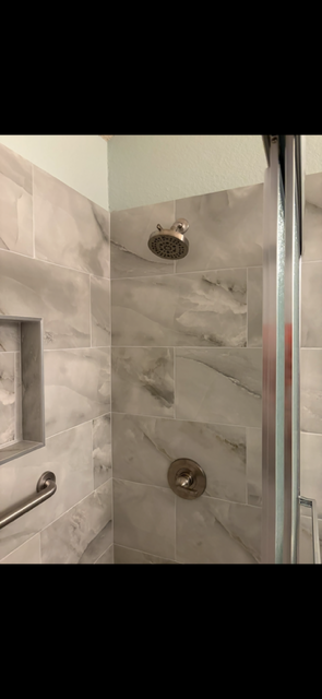 Modern walk-in shower with marble-look tile, rainfall showerhead, recessed niche, and glass door