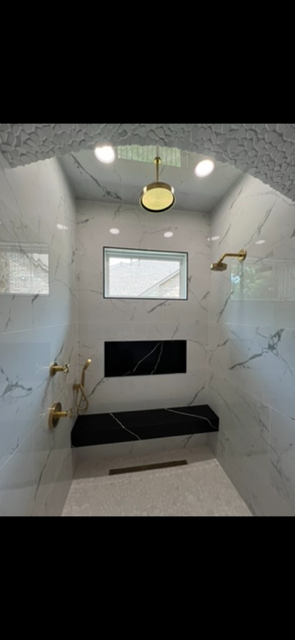 Luxurious marble-tiled shower with rain showerhead, handheld sprayer, gold fixtures, recessed bench, and windows
