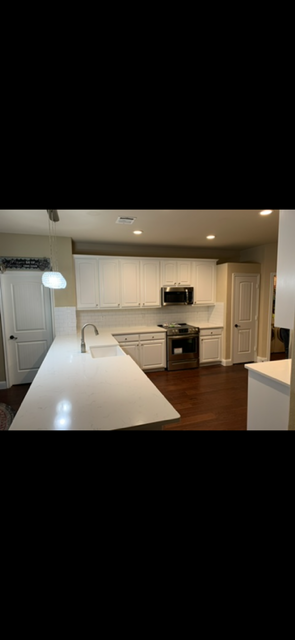 Bright white kitchen with island, farmhouse sink, stainless steel appliances, and hardwood floors