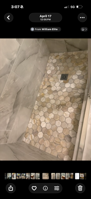 Bathroom shower floor with hexagonal beige and gray mosaic tiles, a centered drain, and large marble-look wall tiles.