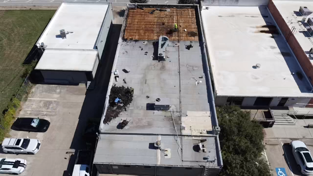 Aerial view of flat-roofed commercial buildings and parking lots, including a damaged rooftop with exposed wooden decking.