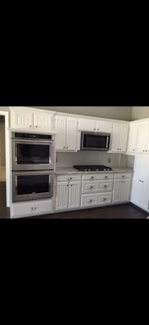 White built-in kitchen cabinetry with double wall ovens, microwave, cooktop, drawers, and a corner refrigerator cabinet.