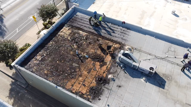 Aerial view of a burned commercial rooftop with charred debris, damaged roofing, and workers inspecting the fire damage.