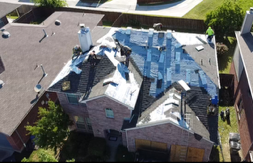 Aerial view of a residential house with blue roofing under construction and workers on the roof.