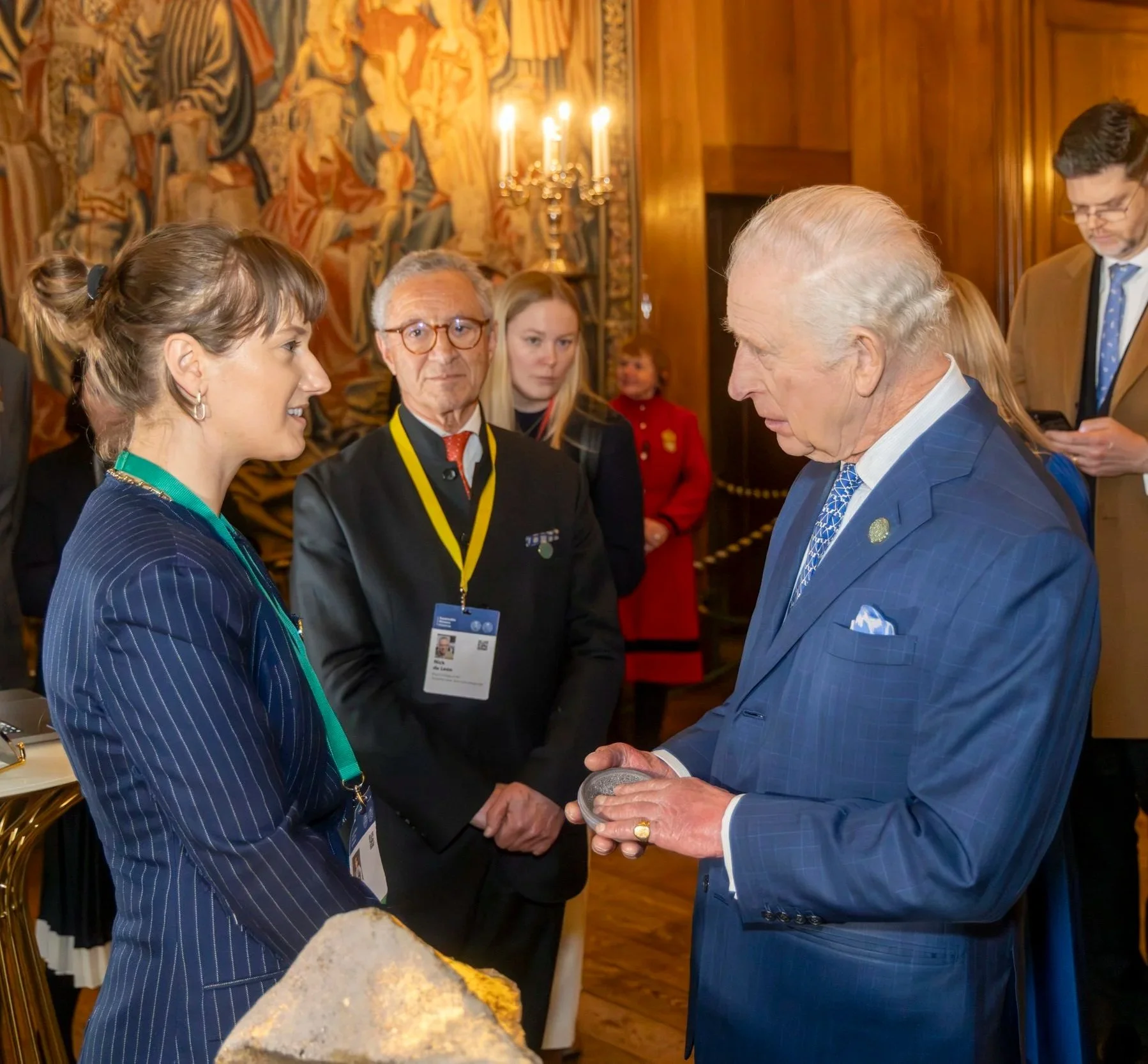 Felicia Neuhof and King Charles III meet at Hampton Court Palace at the Terra Carta Design Lab Round Tables and Exhibition. The setting features Shellf Life bowl, wooden walls, a tapestry, and a candelabrum in the background.
