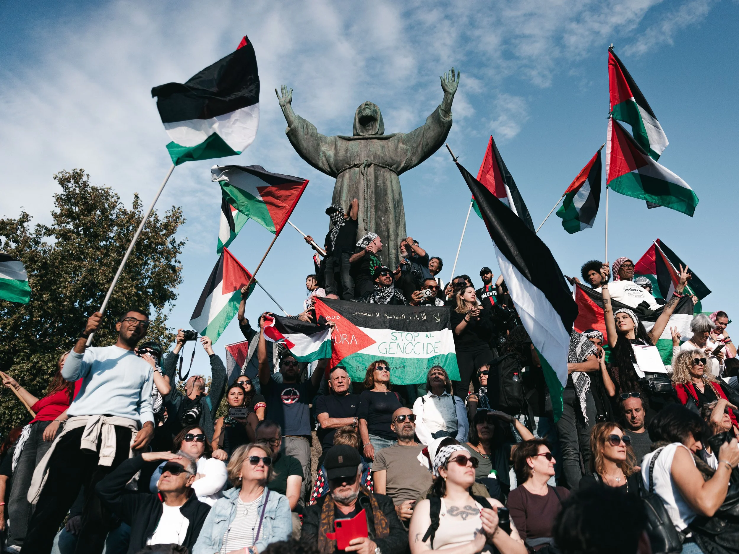 Protesters stand on the Monument to St. Francis of Assisi while waving numerous Palestinian flags, one of which reads “Stop all genocide,” in Rome, Italy on October 4, 2025. The rally is part of nationwide pro-Palestinian demonstrations following Isr