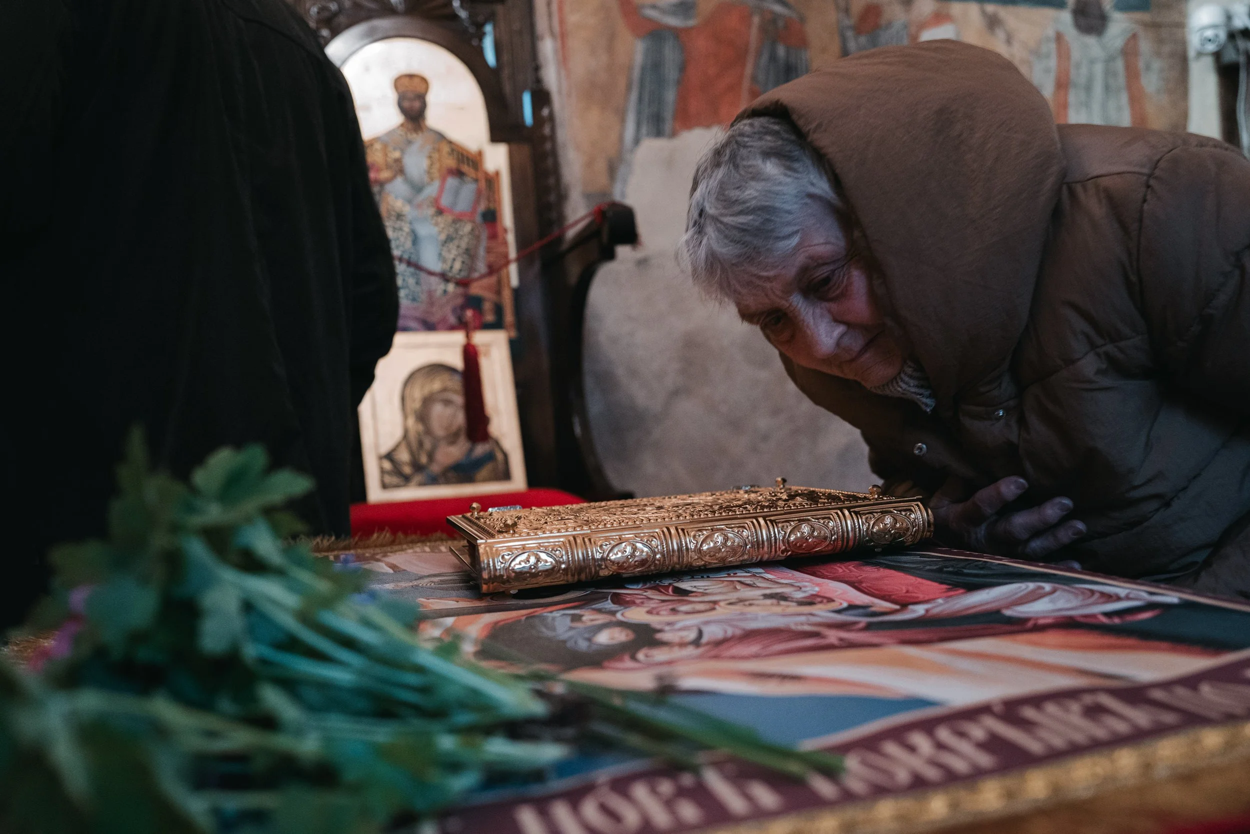 A woman bows her head to kiss a gilded book of sacred texts placed above the Holy Shroud laid upon a table before passing under it during the morning liturgy in Iskrets, Bulgaria on April 10, 2026. The scene is part of the Orthodox Good Friday servic