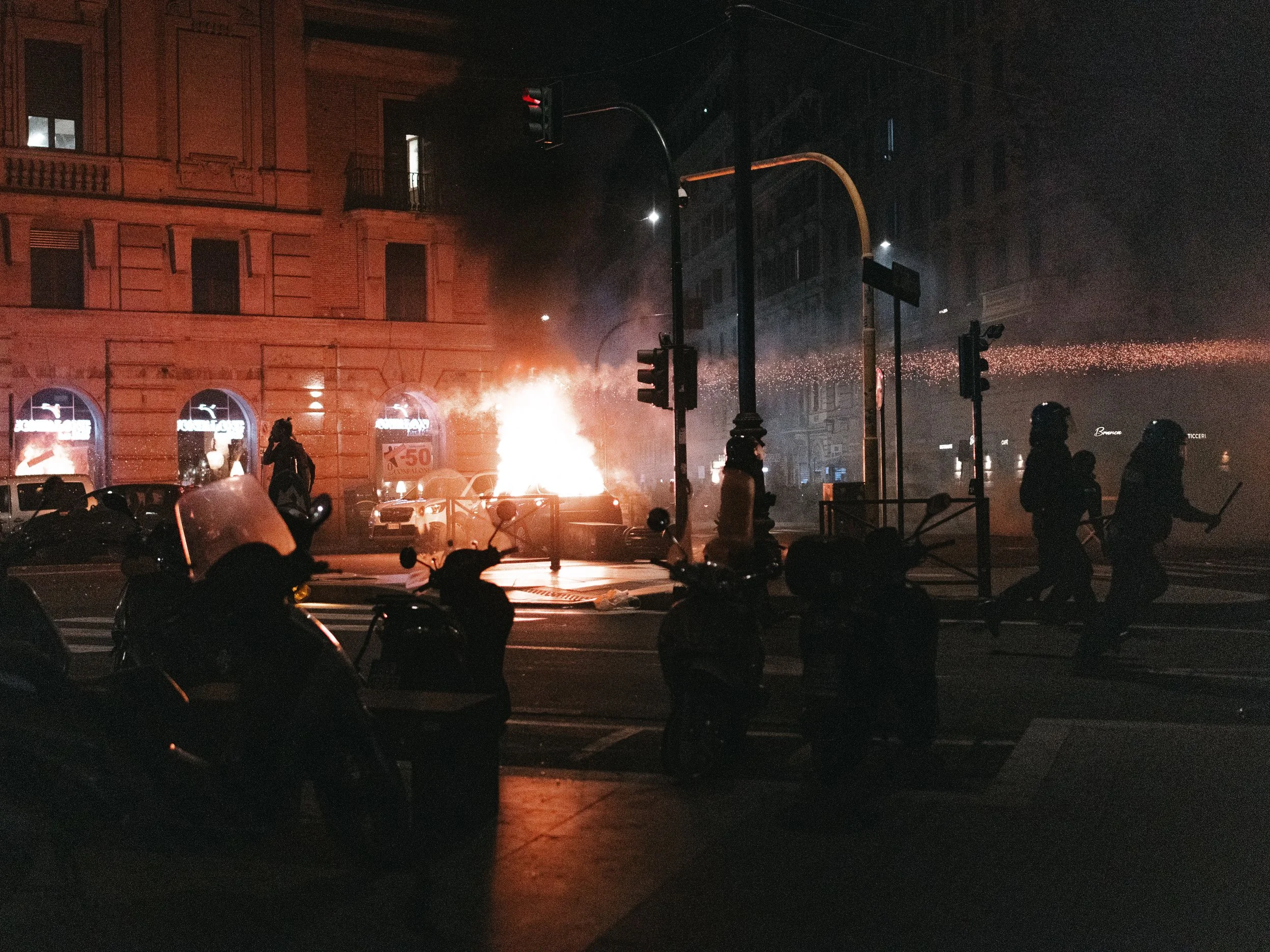 Protesters create a barricade with a burning car and trash bins on a crossroad as police officers run toward them and throw tear gas, forming a line in the picture, in Rome, Italy on October 4, 2025. The scene occurs during nationwide pro-Palestinian