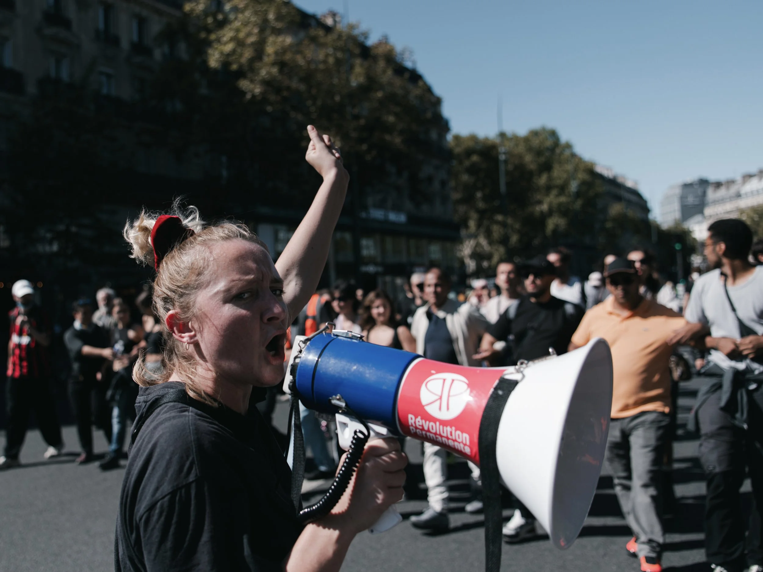 A woman chants with a speaker in front of protesters marching from Gare du Nord during the national strike in Paris, France on September 18, 2025.