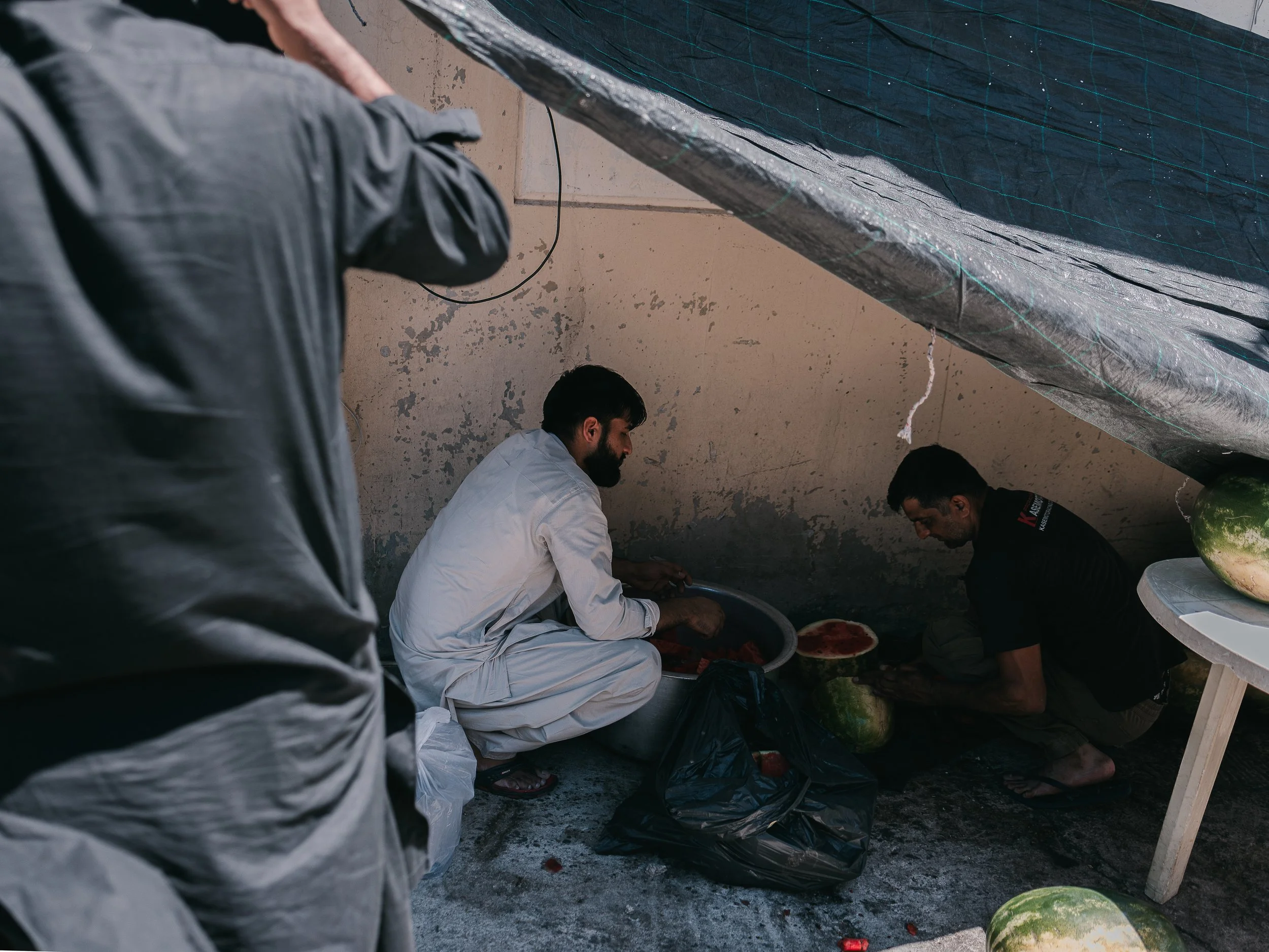Men cut watermelons outside the self-organized Shi’a mosque in Peristeri, Athens, Greece on July 6, 2025. The activity is part of the Ashura preparations, providing food and drinks for participants commemorating the martyrdom of Imam Husayn.