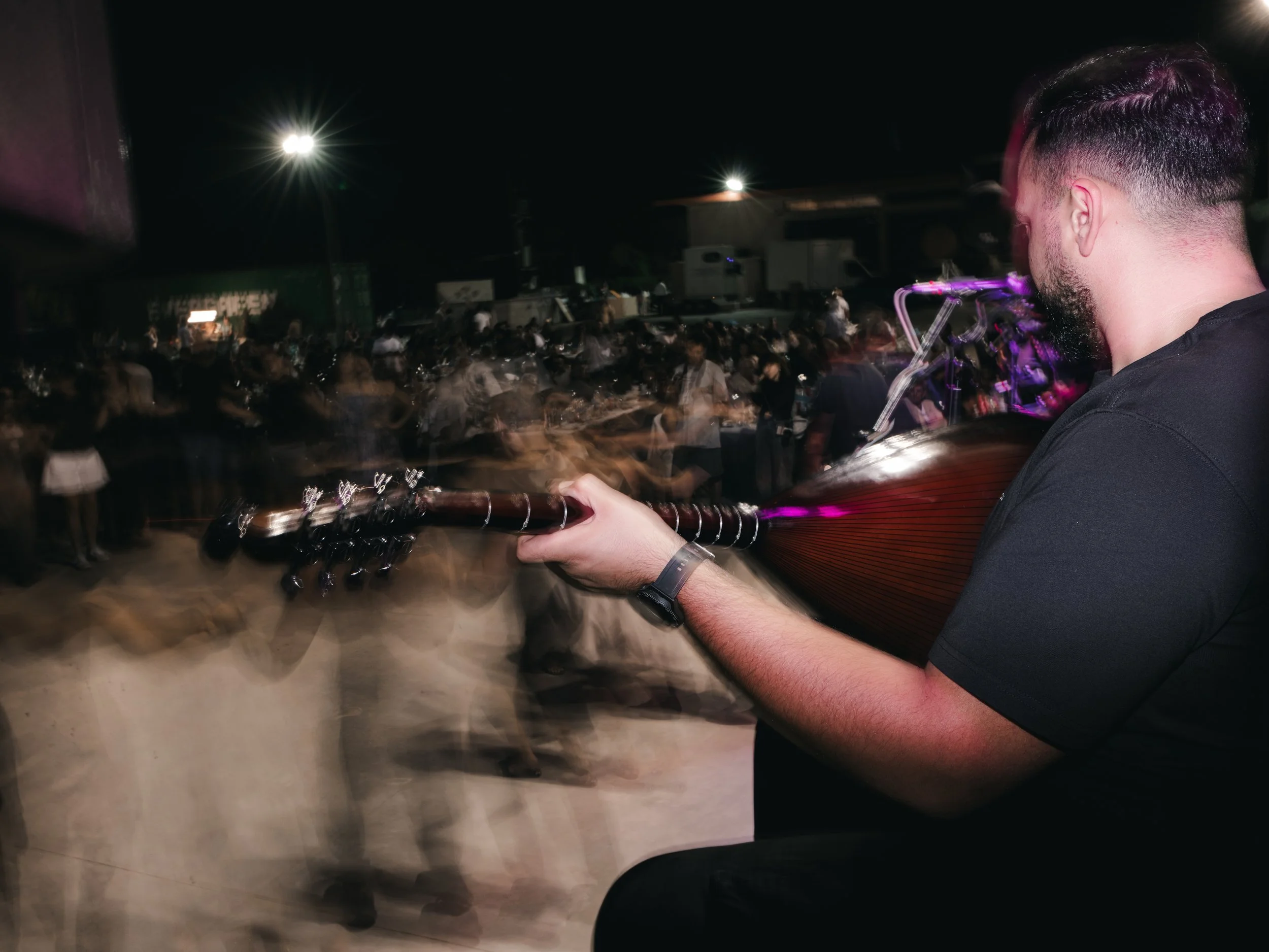 A musician performs as people in traditional Cretan costumes dance in front during a panigiri, a village festival featuring music, food and dance that is rooted in Orthodox religious celebrations and local traditions. Skines, Crete, Greece, August 21