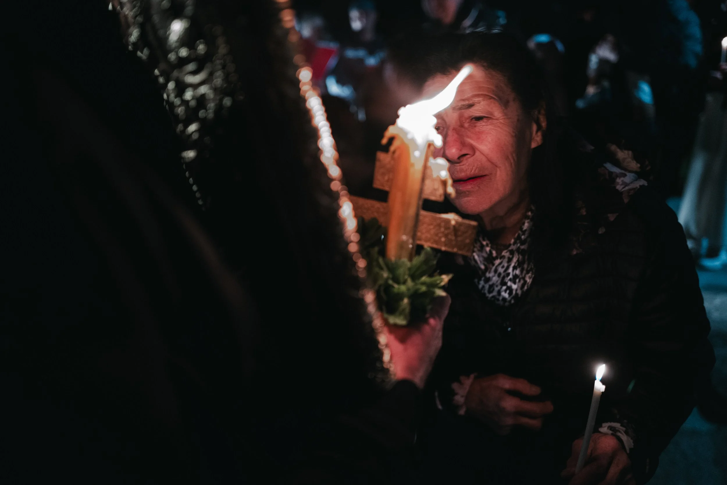 An elderly woman bends to kiss a wooden cross with lit candles, during an Easter service in Iskrets, Bulgaria on April 12, 2026. The scene is part of Orthodox Christian celebrations of the Resurrection of Jesus Christ.