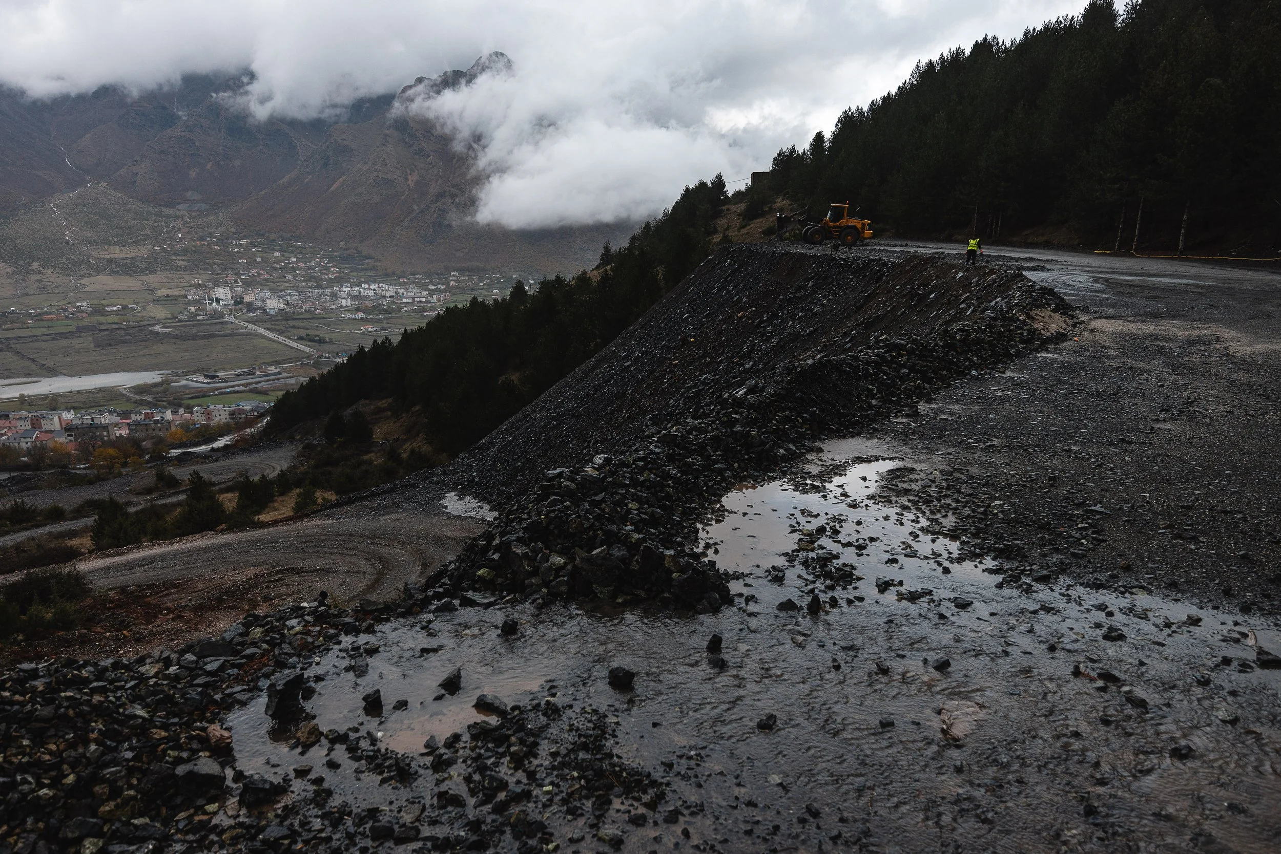 A woman works along the path to the mine where chromium is being cleaned and crushed, with a truck visible nearby in Bulqizë, Dibër County, Albania on November 11, 2025. The scene illustrates the hands-on processing of chromium ore before it is trans