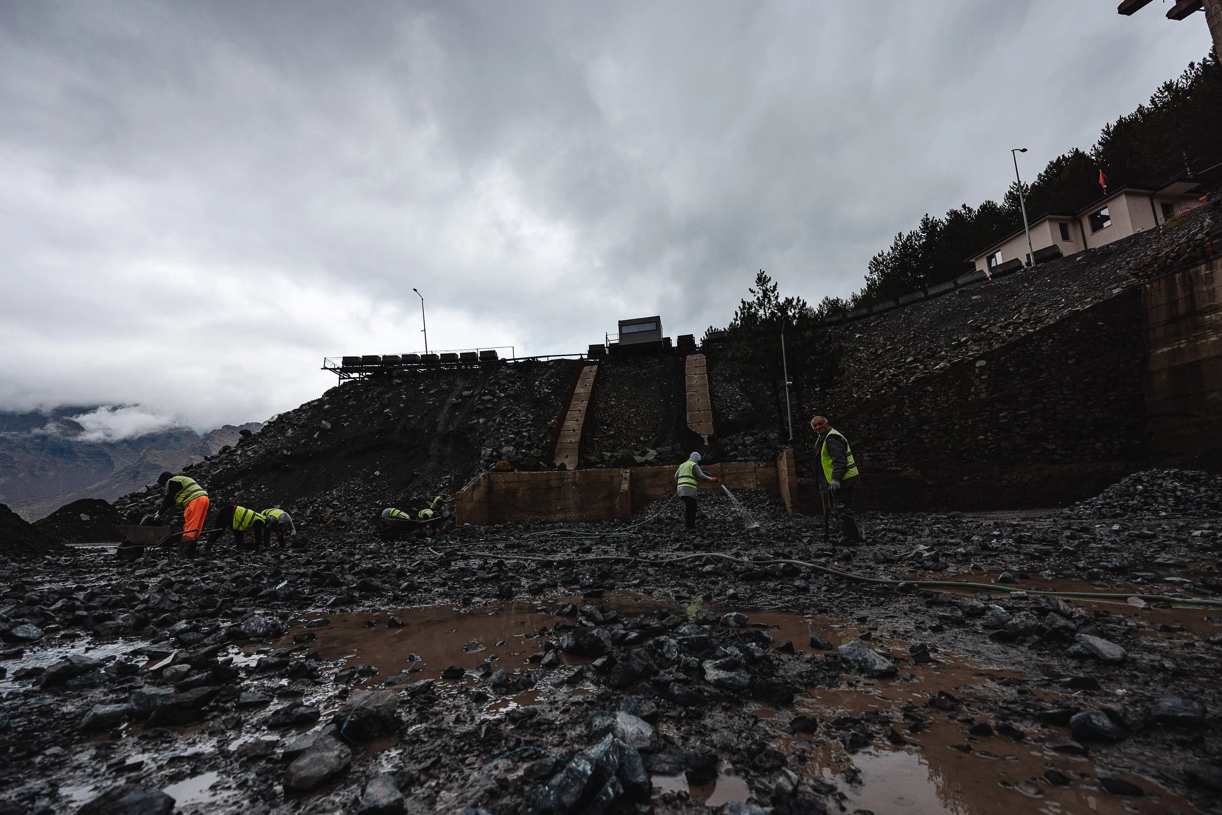 Men and women wet and hammer chromium ore on a large platform in front of the mine in Bulqizë, Dibër County, Albania on November 11, 2025. This activity is part of the ore beneficiation process: crushing and washing the chromite to separate valuable 
