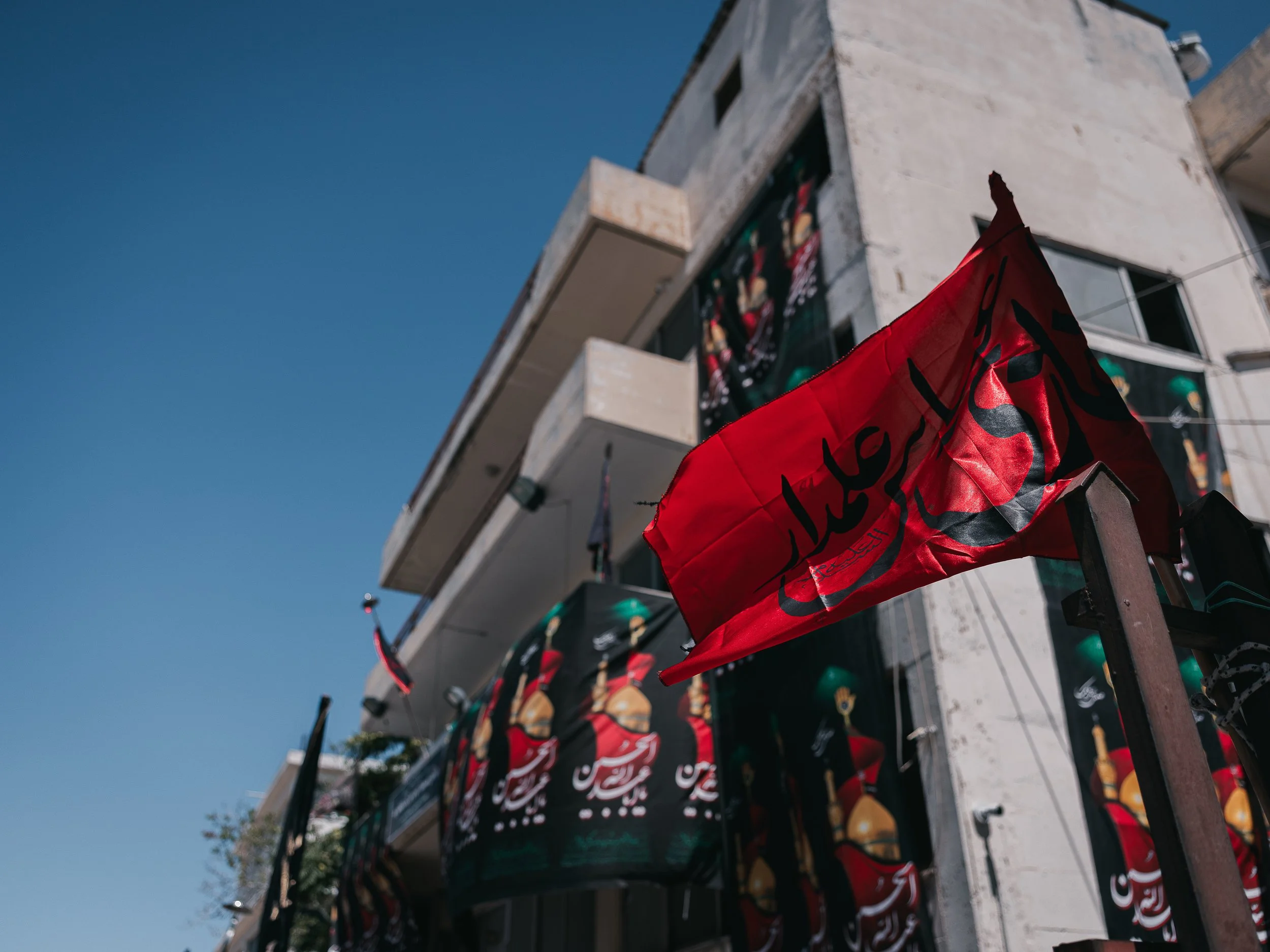 A red flag with black inscriptions waves in front of the self-organized Shi’a mosque in Peristeri, Athens, Greece on July 6, 2025. The flag is a Husseini banner, symbolizing mourning and remembrance of Imam Husayn’s martyrdom at Karbala during the As