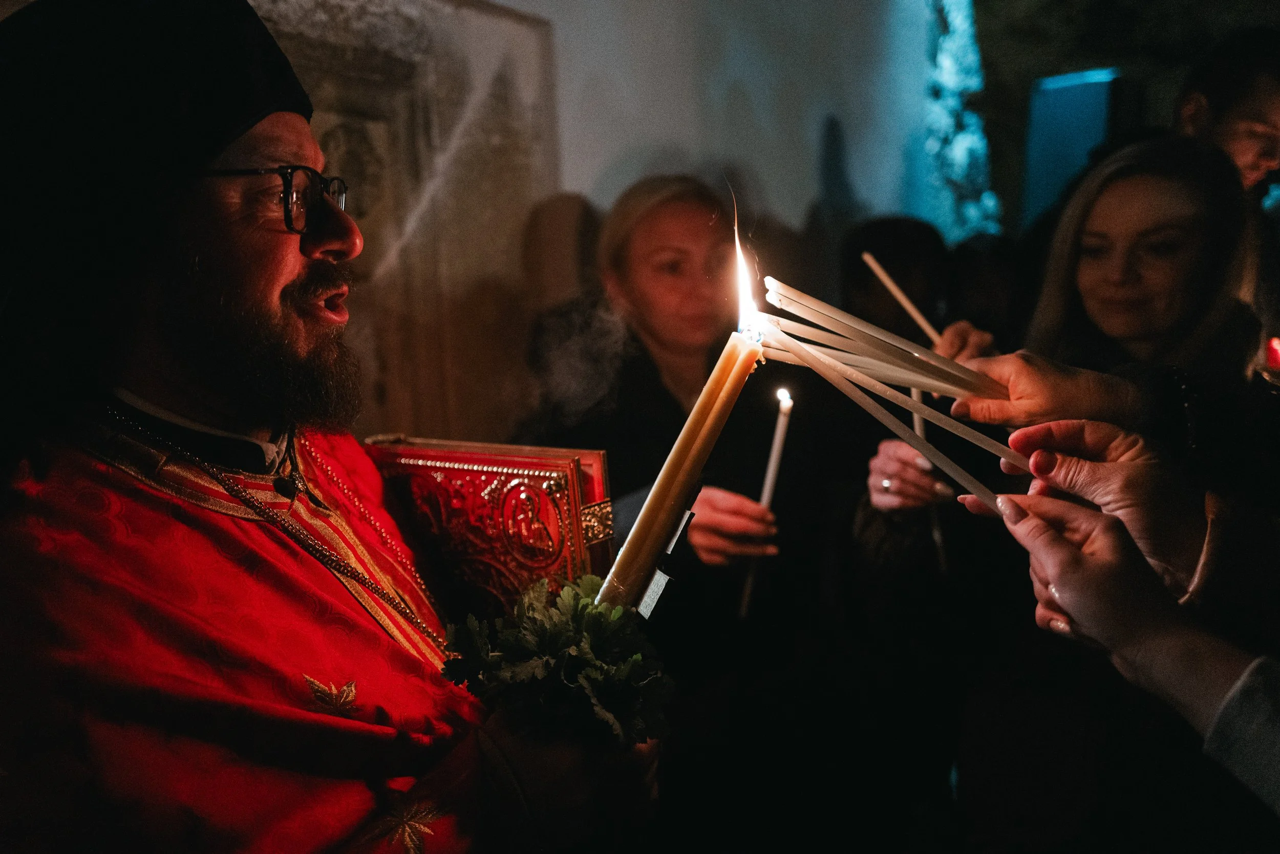 Archimandrite Januarij holds a lit candle from which worshippers light their own candles with the Holy Fire in Iskrets, Bulgaria on April 12, 2026. The scene is part of the Orthodox Easter service, symbolizing the Resurrection of Jesus Christ and the