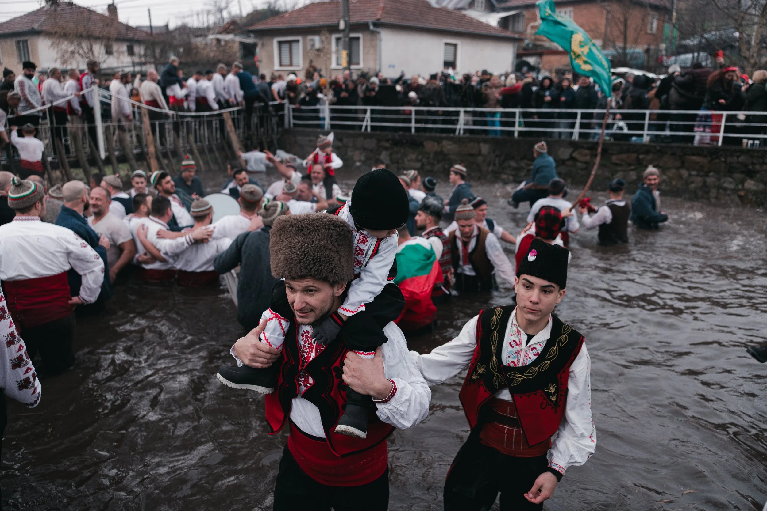 A man in traditional clothing with a child on his shoulders is walking out of the icy Tundzha River after the dance during Epiphany celebrations in Kalofer, Bulgaria on January 6, 2026. Taking part in the dance is considered a symbol of honour, faith