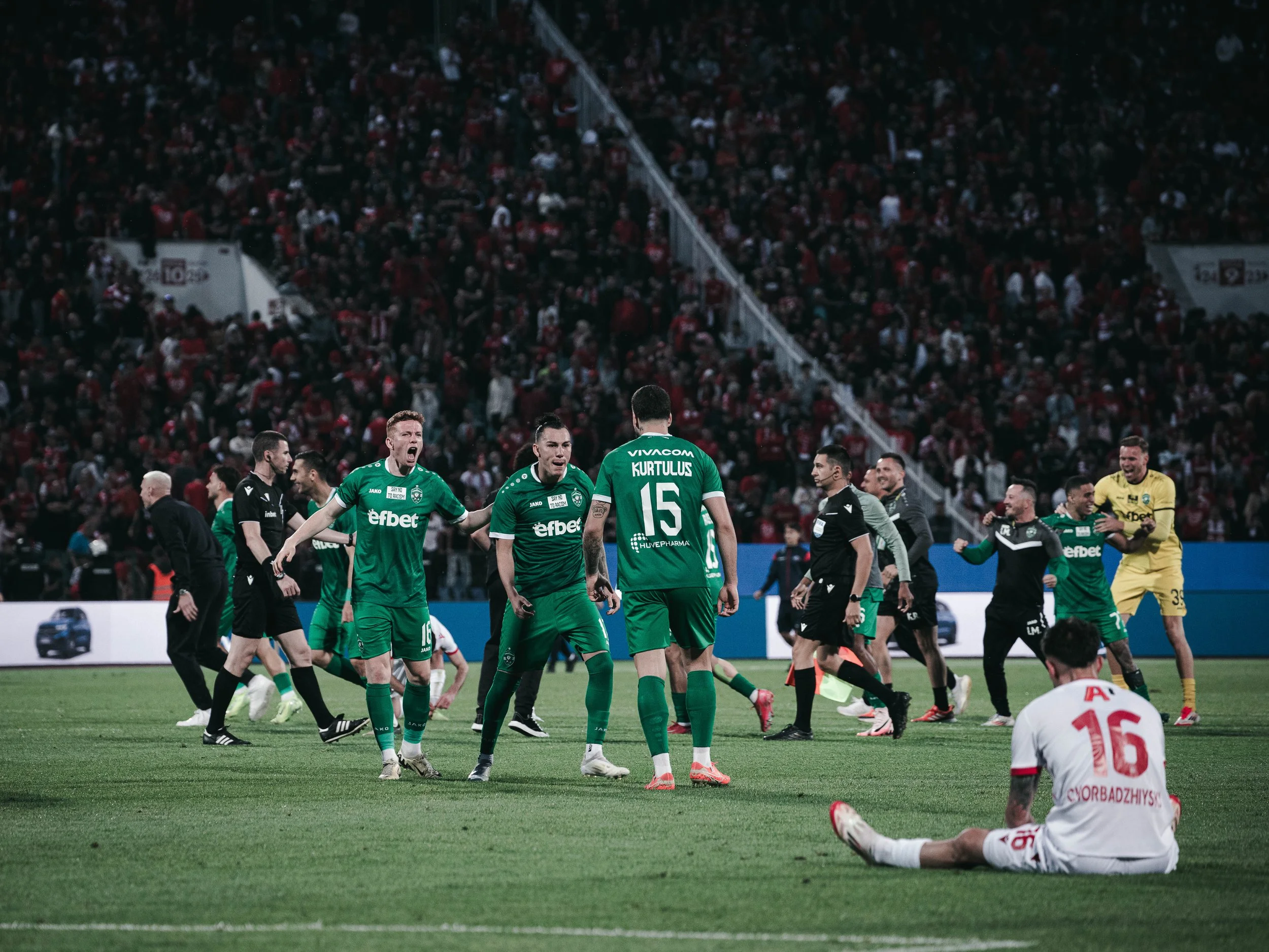 Ludogorets players celebrate wildly as the match ends, running and jumping, while CSKA Sofia’s Georgi Brankov Chorbadzhiyski sits dejected on the ground. Sofia, Bulgaria – May 22, 2025.