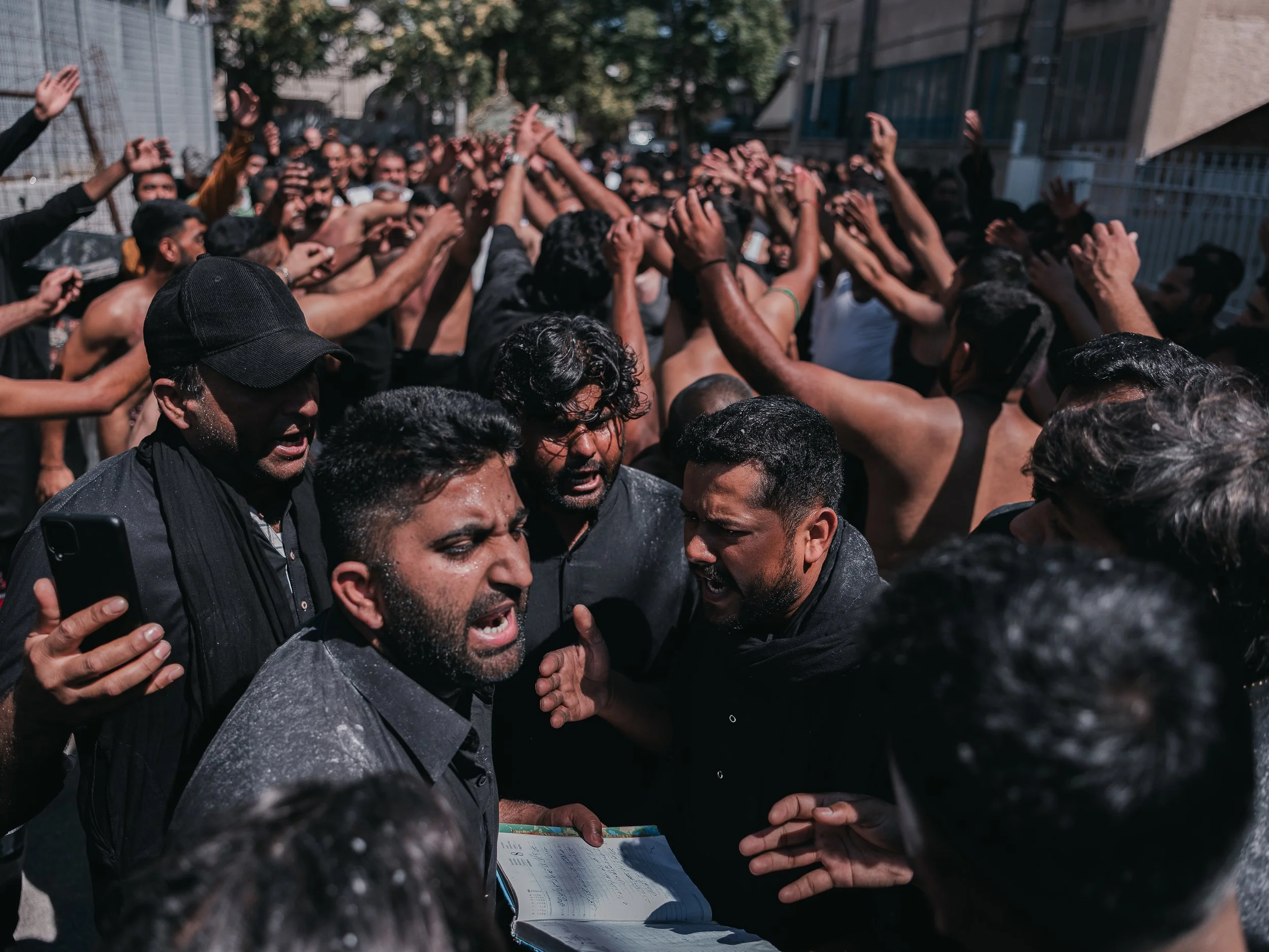 Men chant and perform rhythmic chest-beating while one of them holds a book during their procession in Peristeri, Athens, Greece on July 6, 2025. The ritual, called latm or matam, involves reciting elegies from the book and striking their chests in u