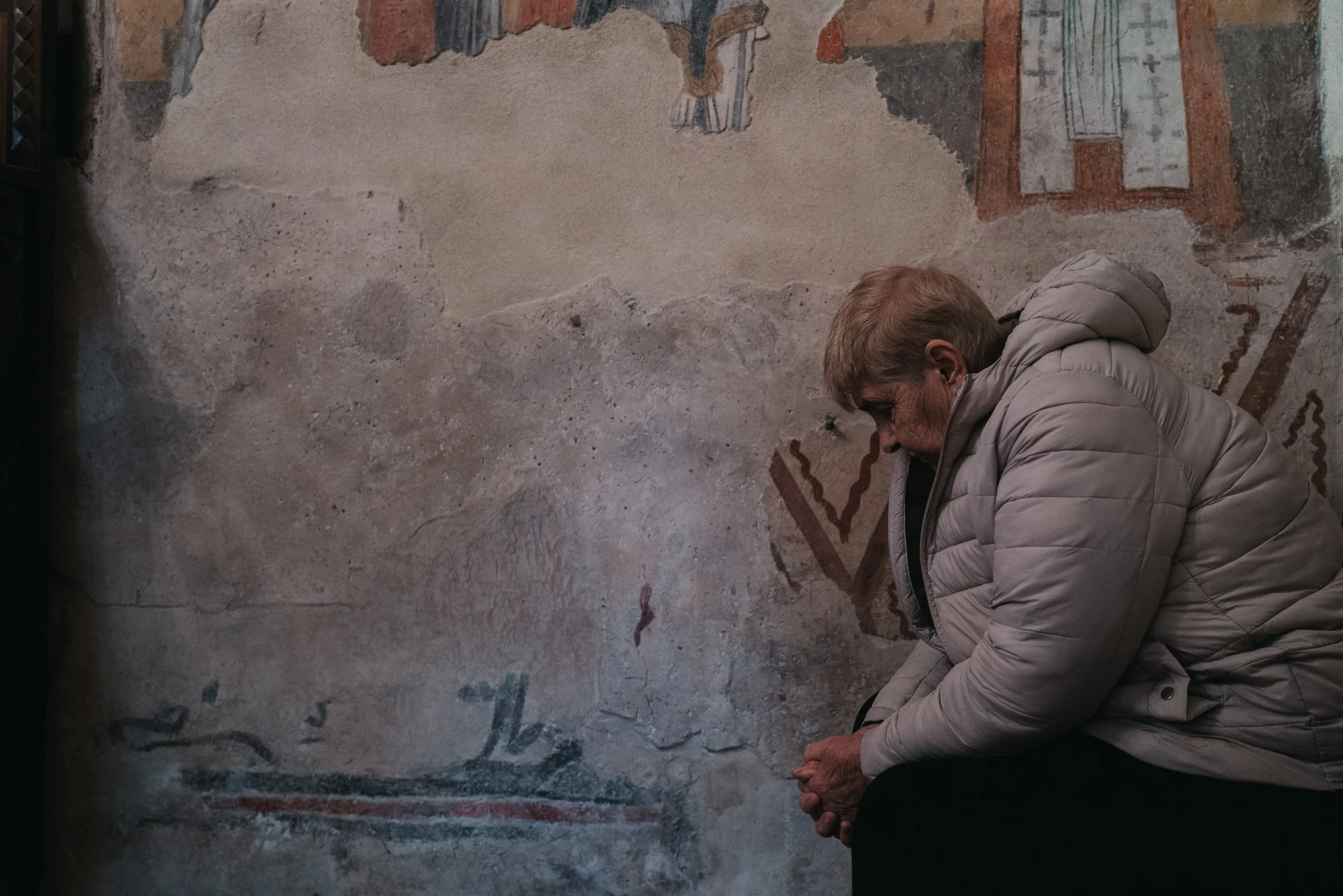 A woman sits with her head bowed and hands clasped during the morning liturgy in the monastery in Iskrets, Bulgaria on April 10, 2026. The scene is part of the Orthodox Good Friday service, reflecting prayer, humility, and personal devotion.