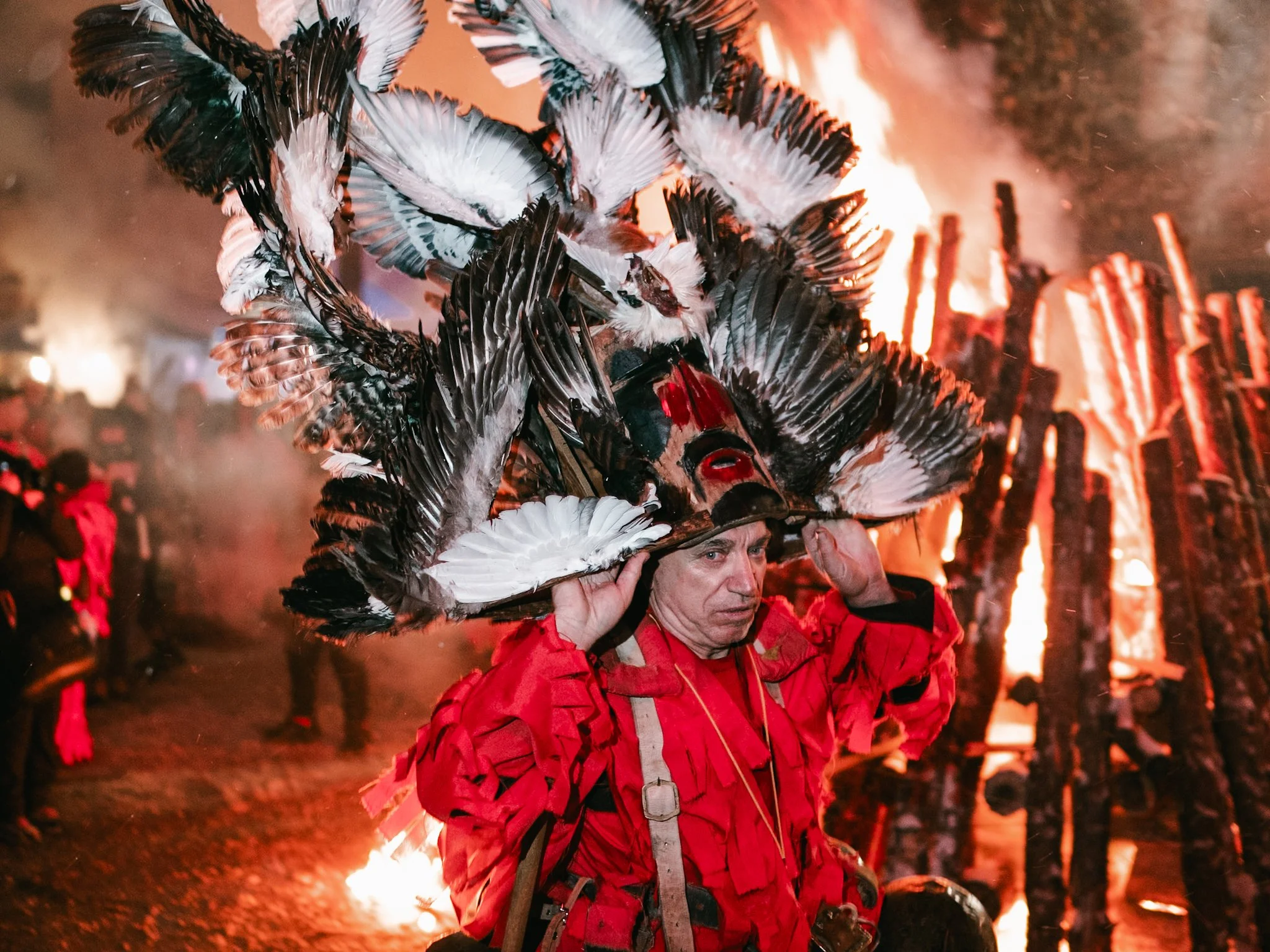 A man, holding a large mask above his head, moves gracefully in front of the Surva fire in Kosharevo, embodying the ancient traditions of the festival, where masks and flames converge to drive away evil spirits and ensure a prosperous year ahead.