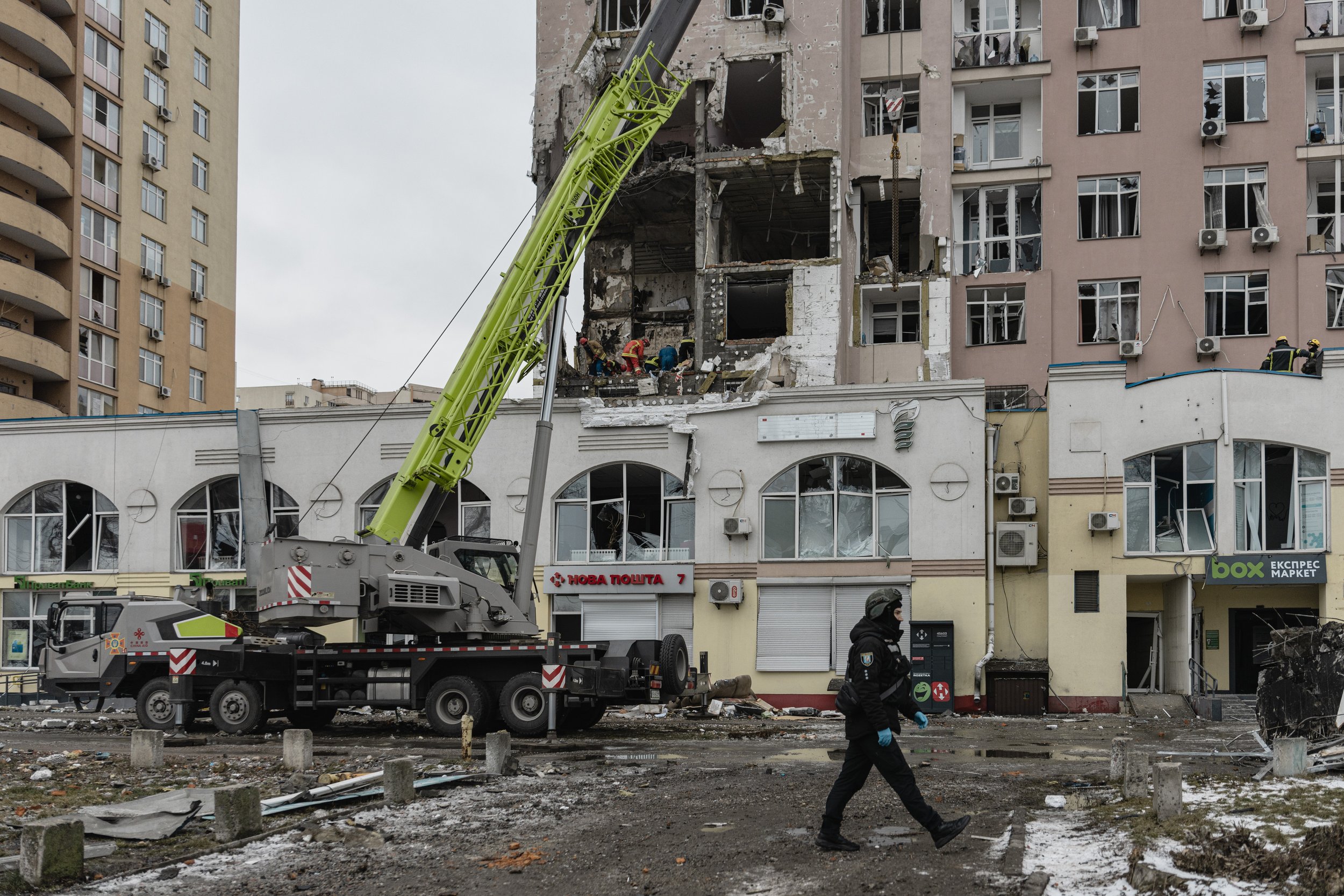 Emergency services clear debris from the struck building on Hotkevycha Street in Kyiv, Ukraine on December 27, 2025. The attack, carried out by a Russian Shahed drone, damaged the lower floors of a high-rise building and injured several civilians.
