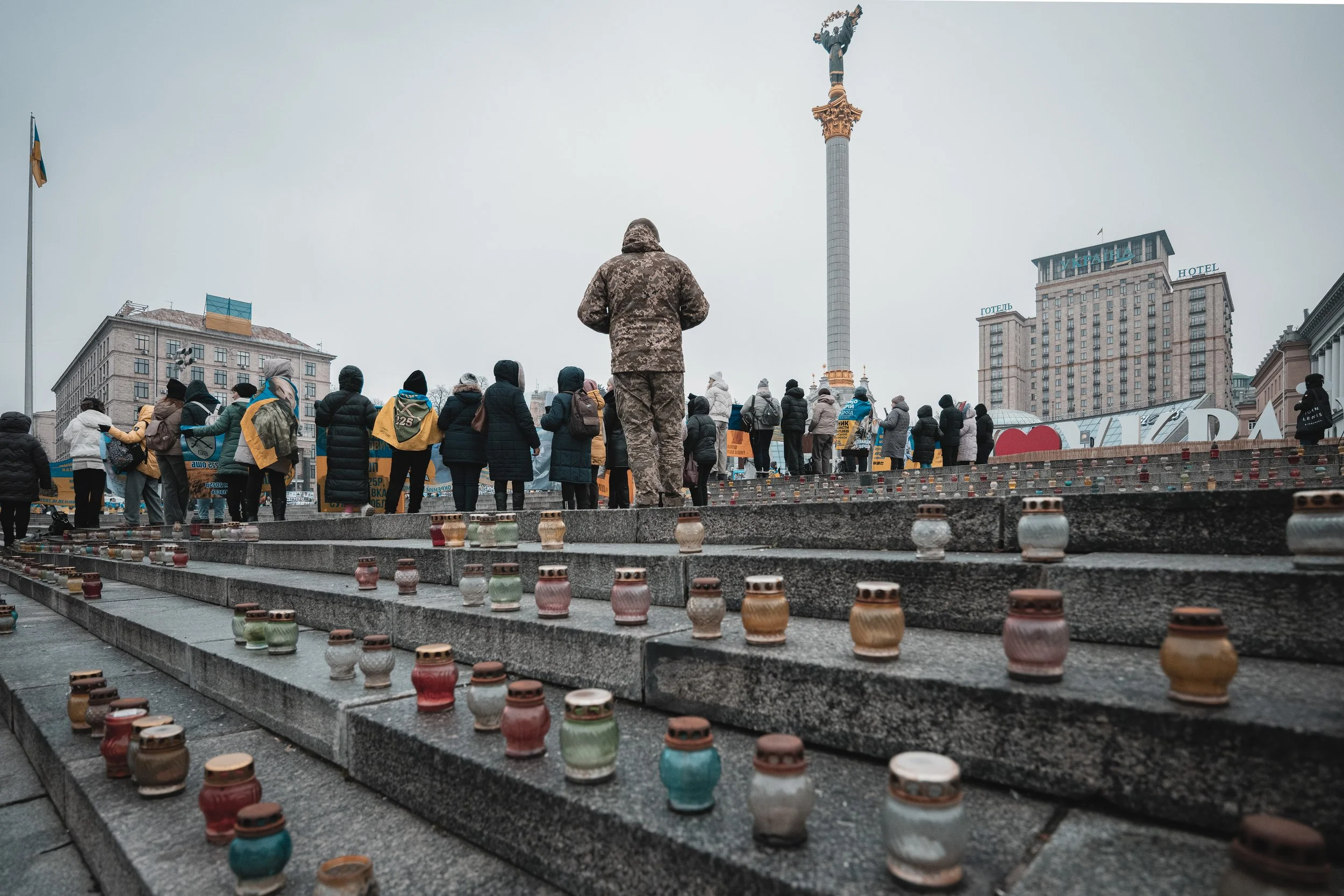 People gather in a circle with candles placed on the stairs behind them at Maidan Square, Kyiv, Ukraine on December 18, 2025. The event marks a vigil for missing and captured Ukrainian soldiers, emphasizing remembrance and urging authorities and inte