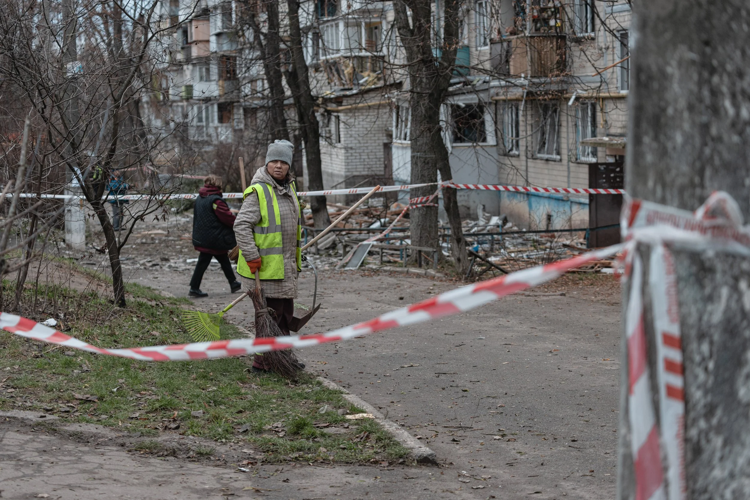 A woman cleans in front of the struck residential building cordoned off with red and white tape in the Sviatoshynskyi district of Kyiv, Ukraine on December 23, 2025. The incident occurred during a Russian aerial strike that partially damaged the buil