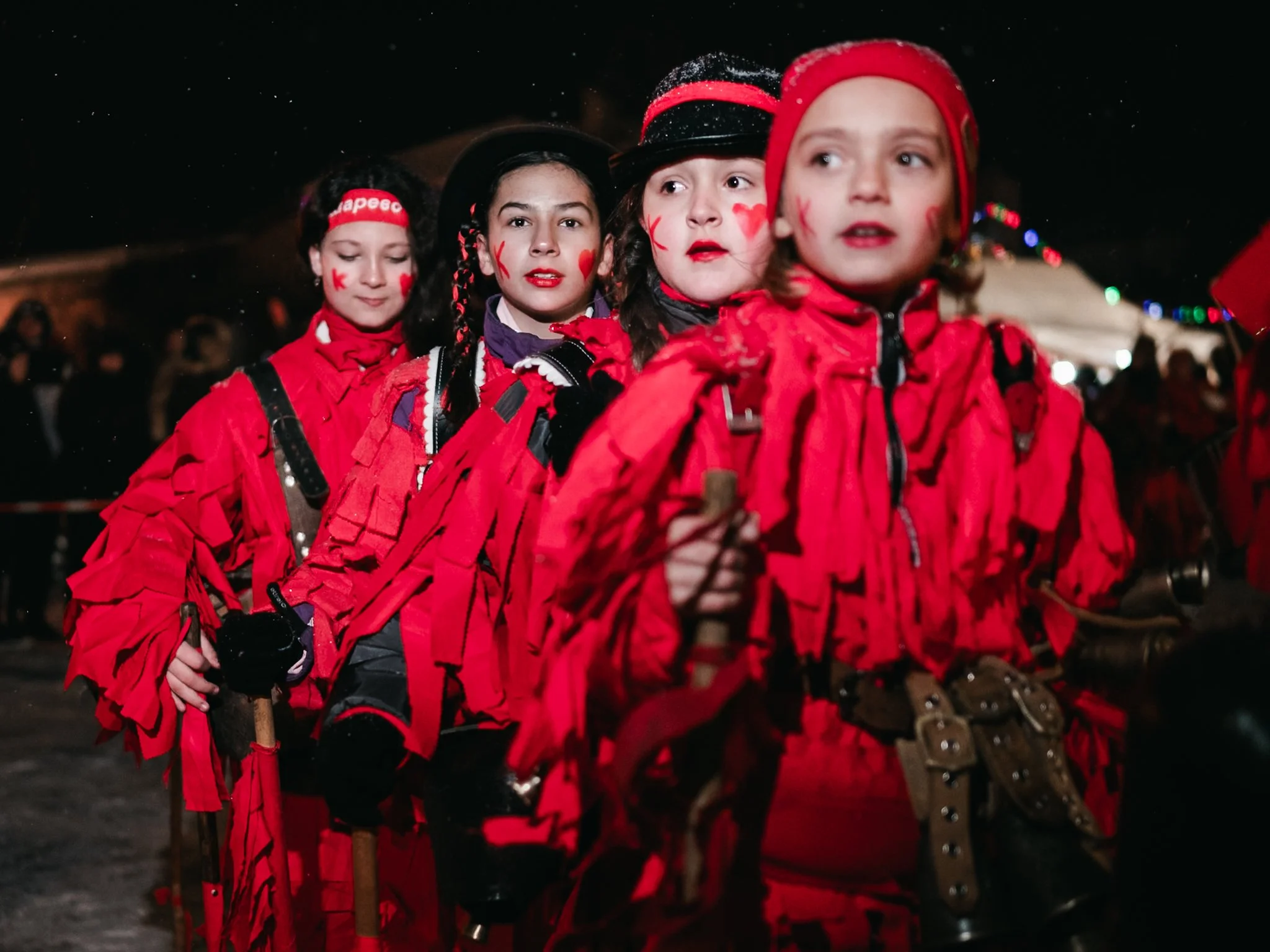 Four girls, clad in striking red costumes with fringe and bells, stand poised and alert, each looking in a different direction as they participate in the time-honored Surva celebration at Kosharevo.