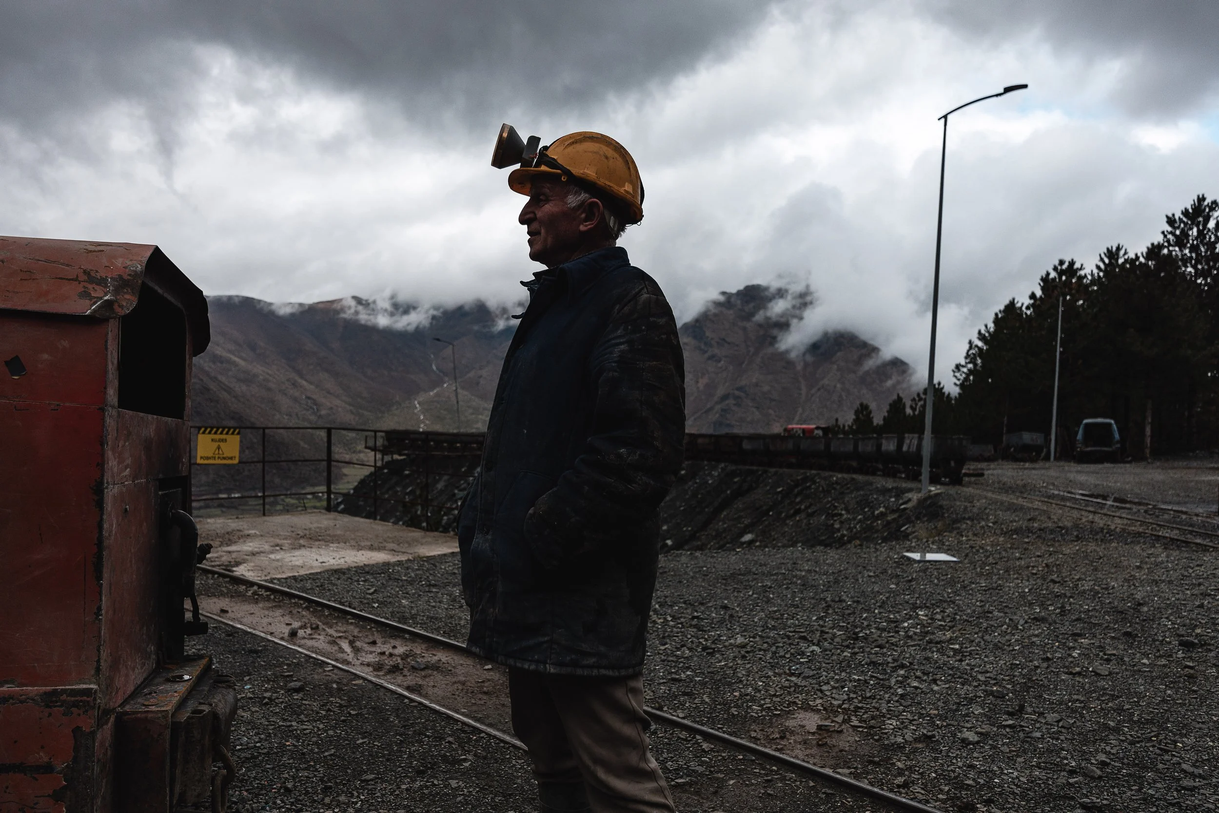 A man stands wearing a helmet in front of the mine in Bulqizë, Dibër County, Albania on November 11, 2025. The image highlights the protective gear worn by miners working in one of Europe’s largest chromium extraction sites.