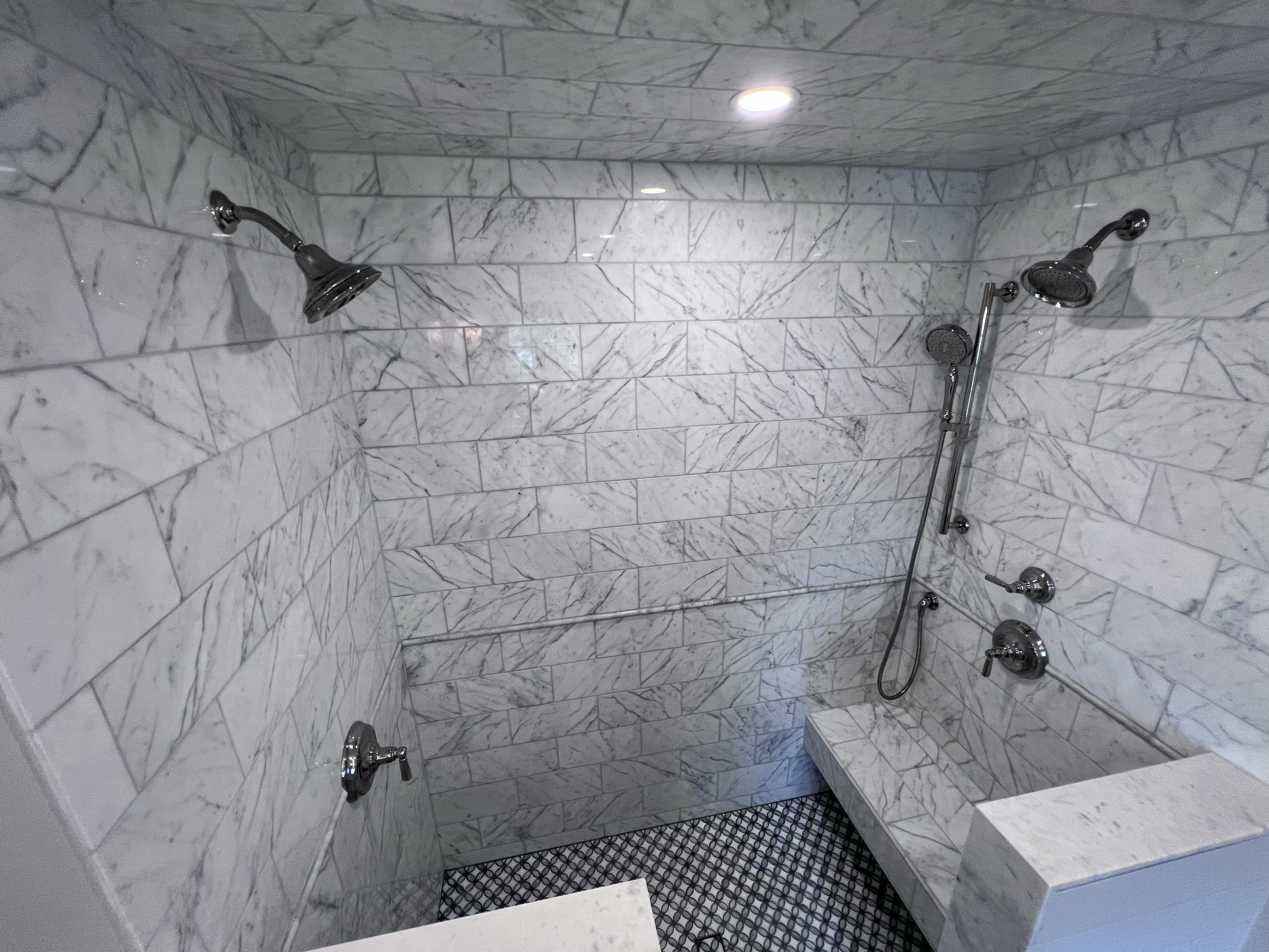 Large marble walk-in shower with marble slab bench and dual shower heads.
