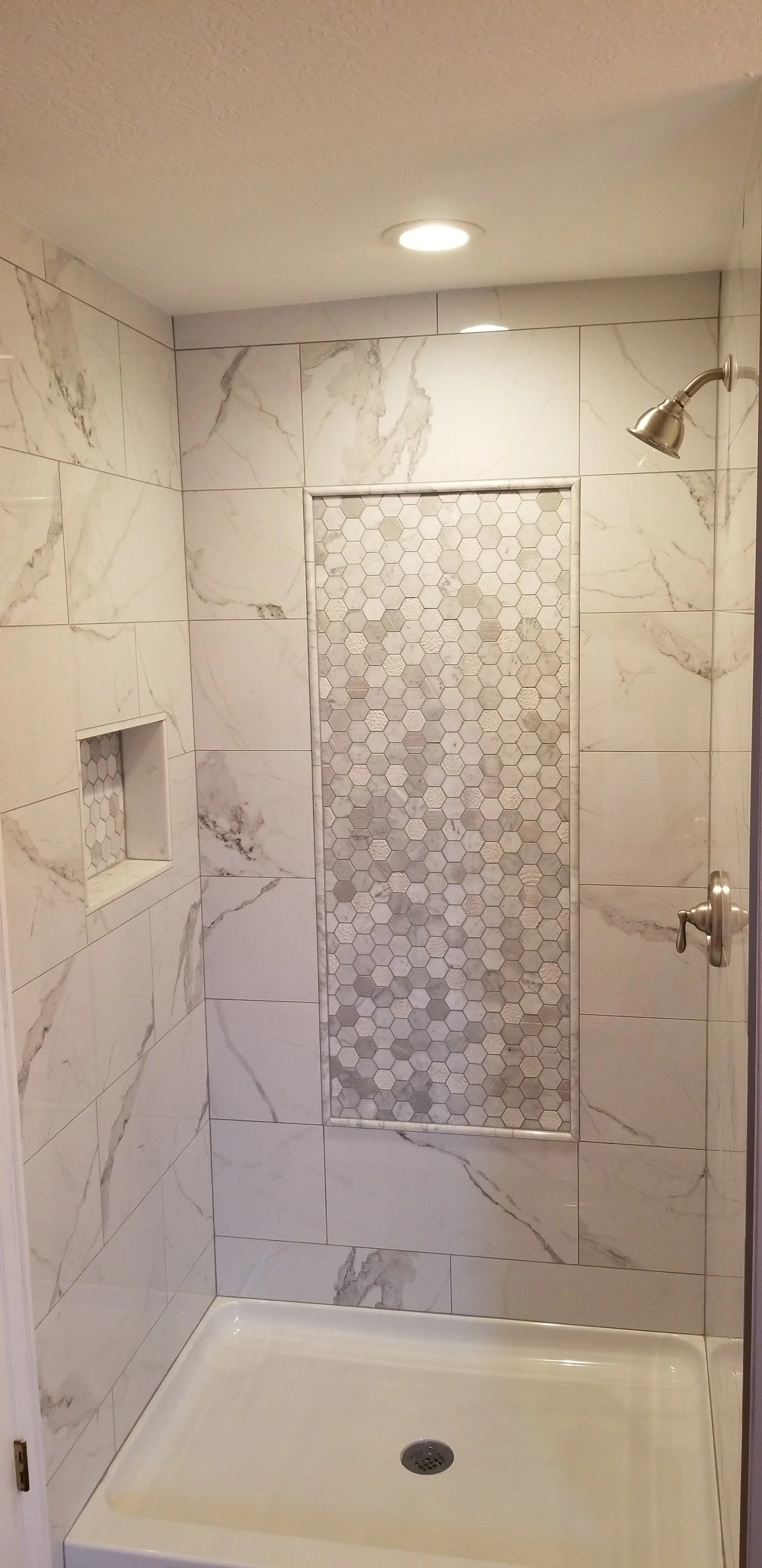 Marble tile shower renovation with custom tile accent.
