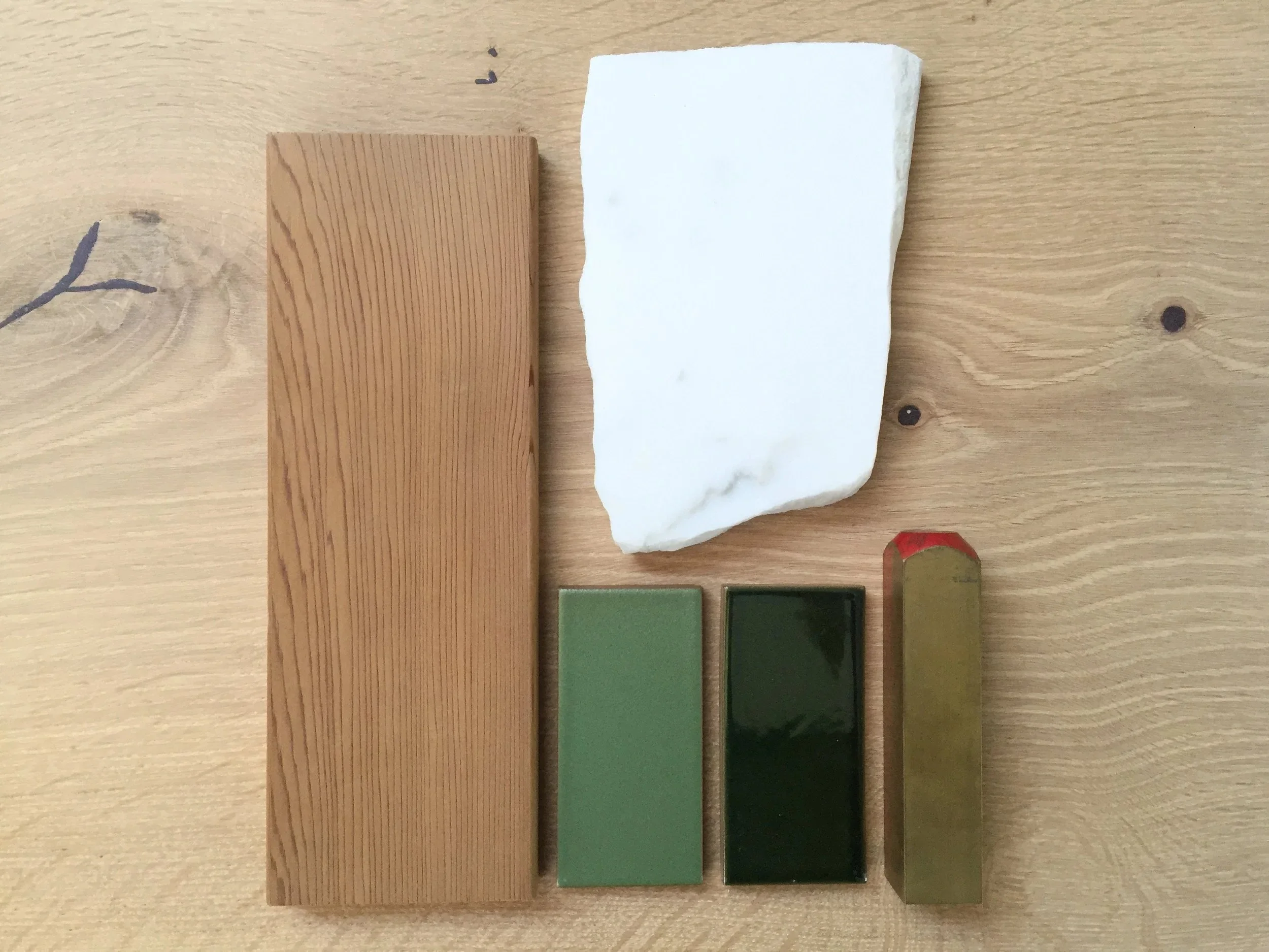 A wooden table with a rectangular wooden block, a white marble slab, and six rectangular blocks painted in different shades of green and black.
