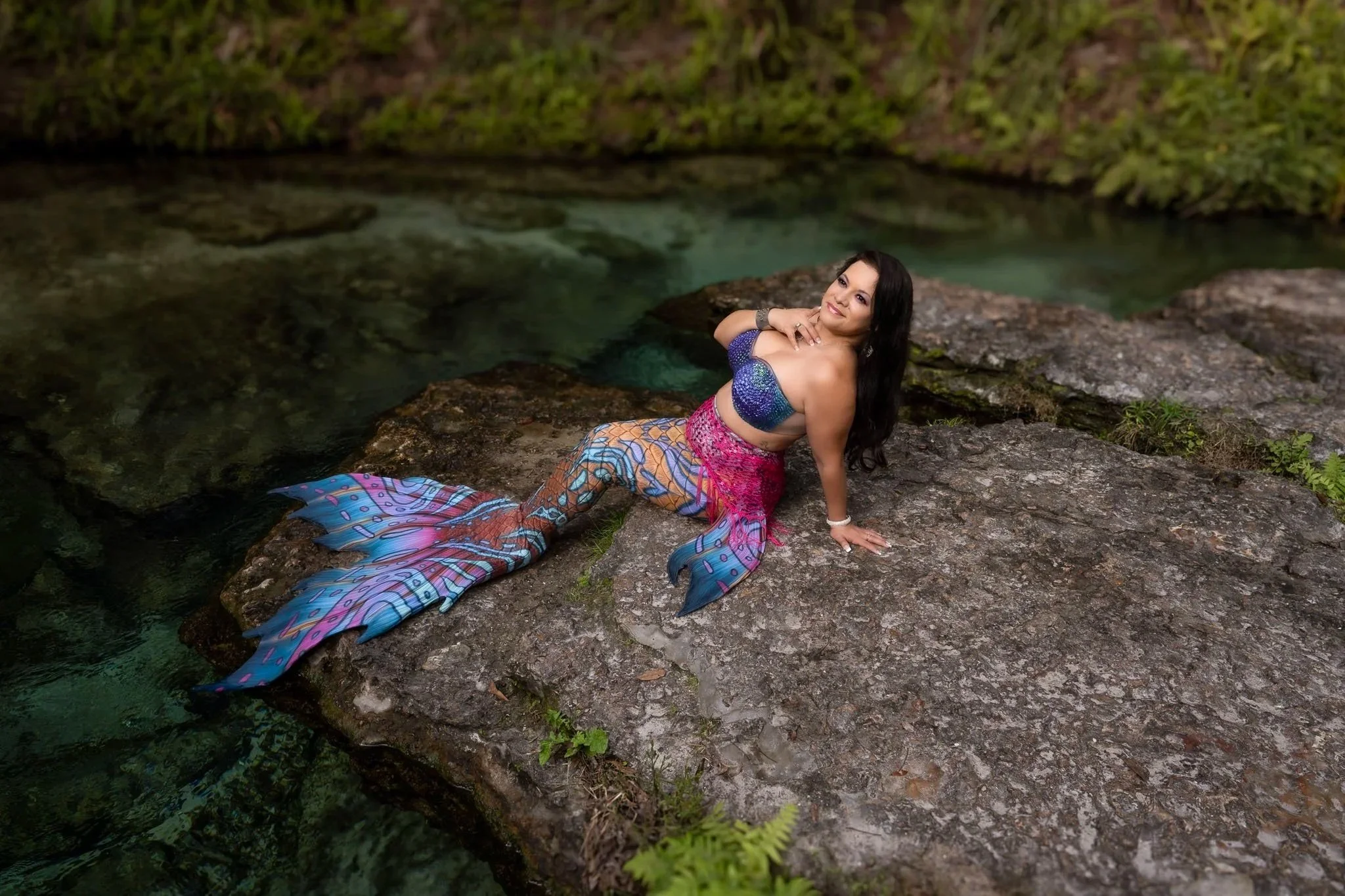 Mermaid poses in the rock in front a flowing clear creek