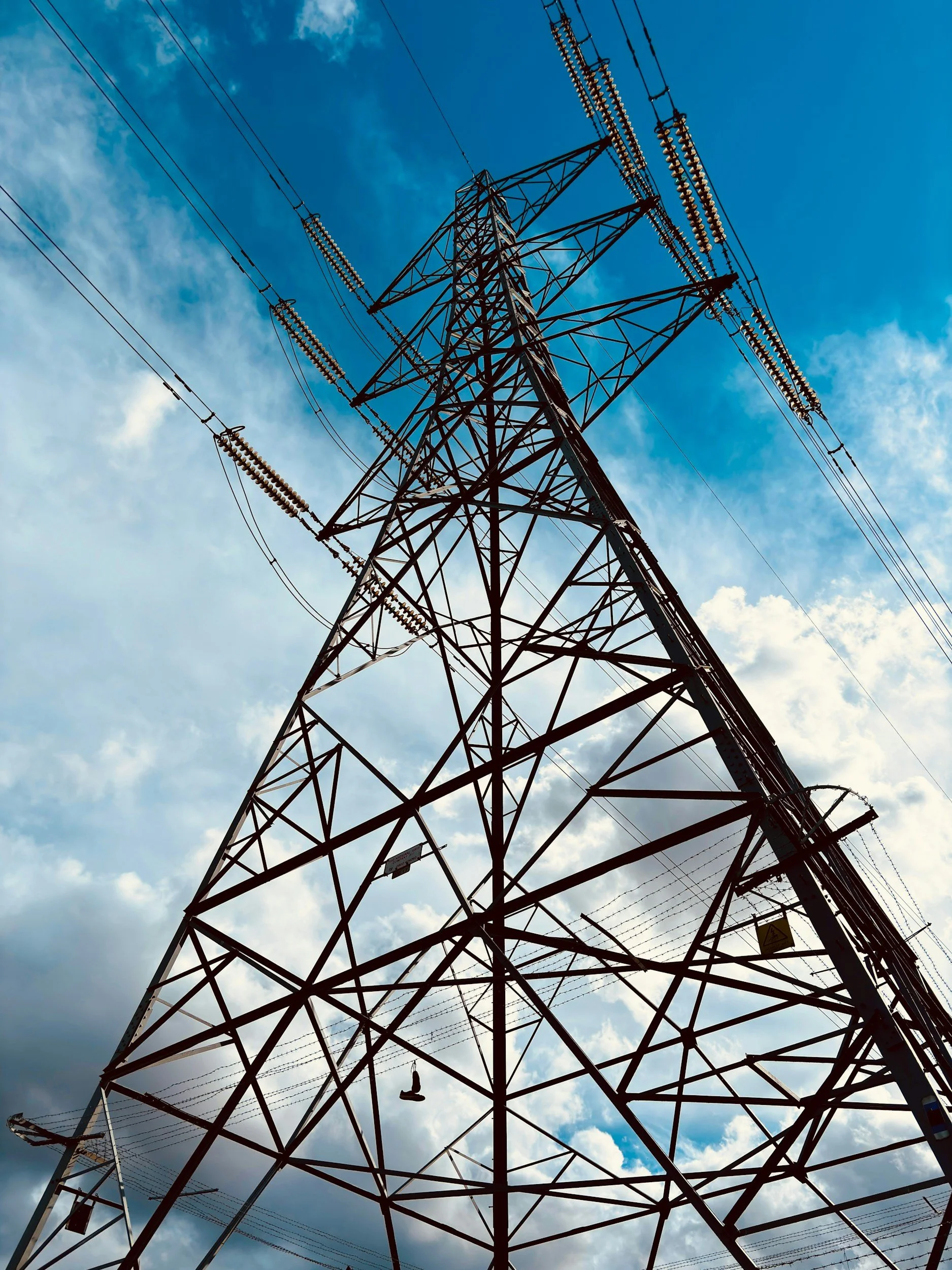 Low-angle view of a tall electricity pylon with power lines against a partly cloudy sky.