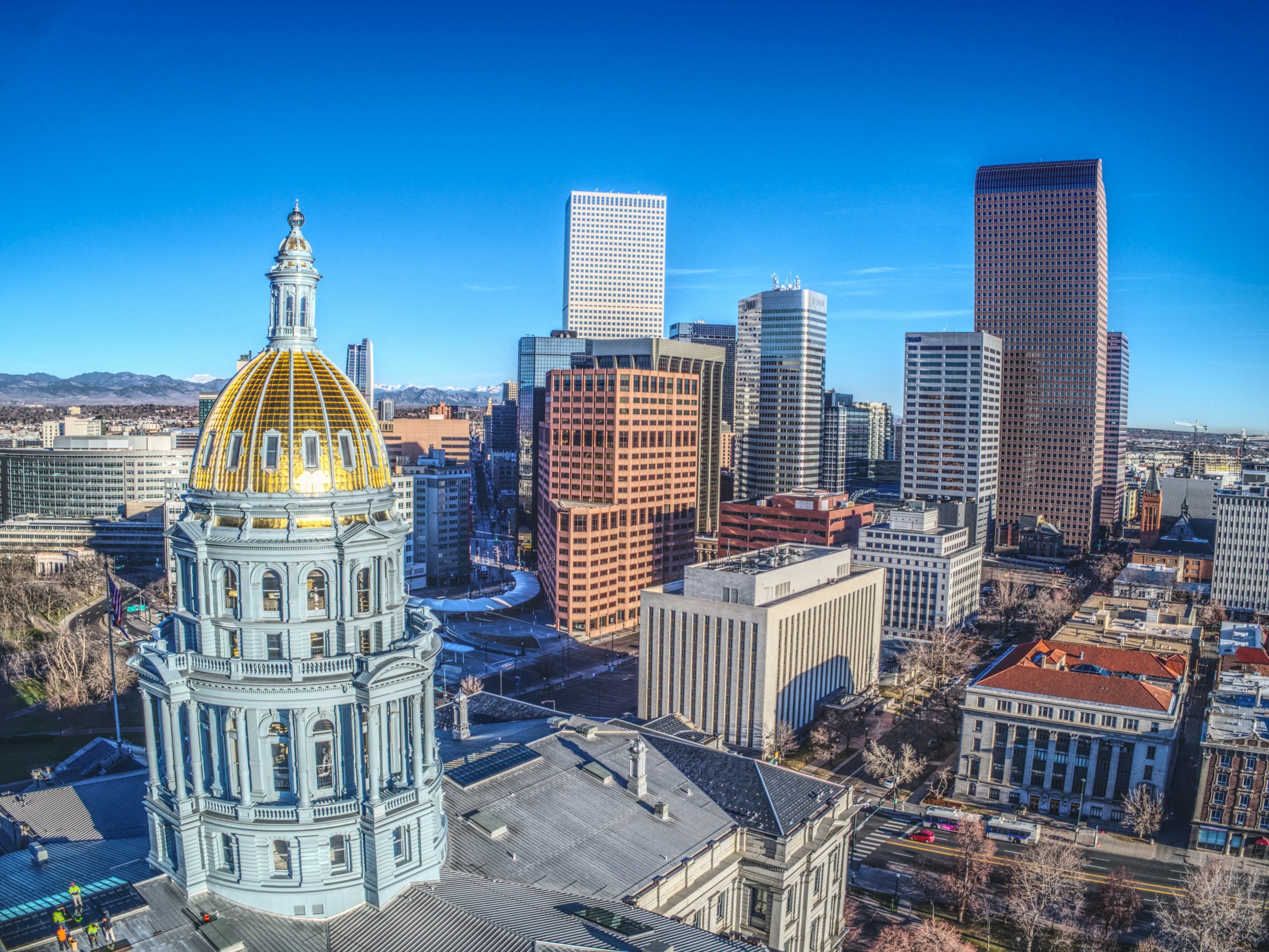 A city skyline featuring a historic building with a gold-domed roof in the foreground, and modern skyscrapers against a clear blue sky.