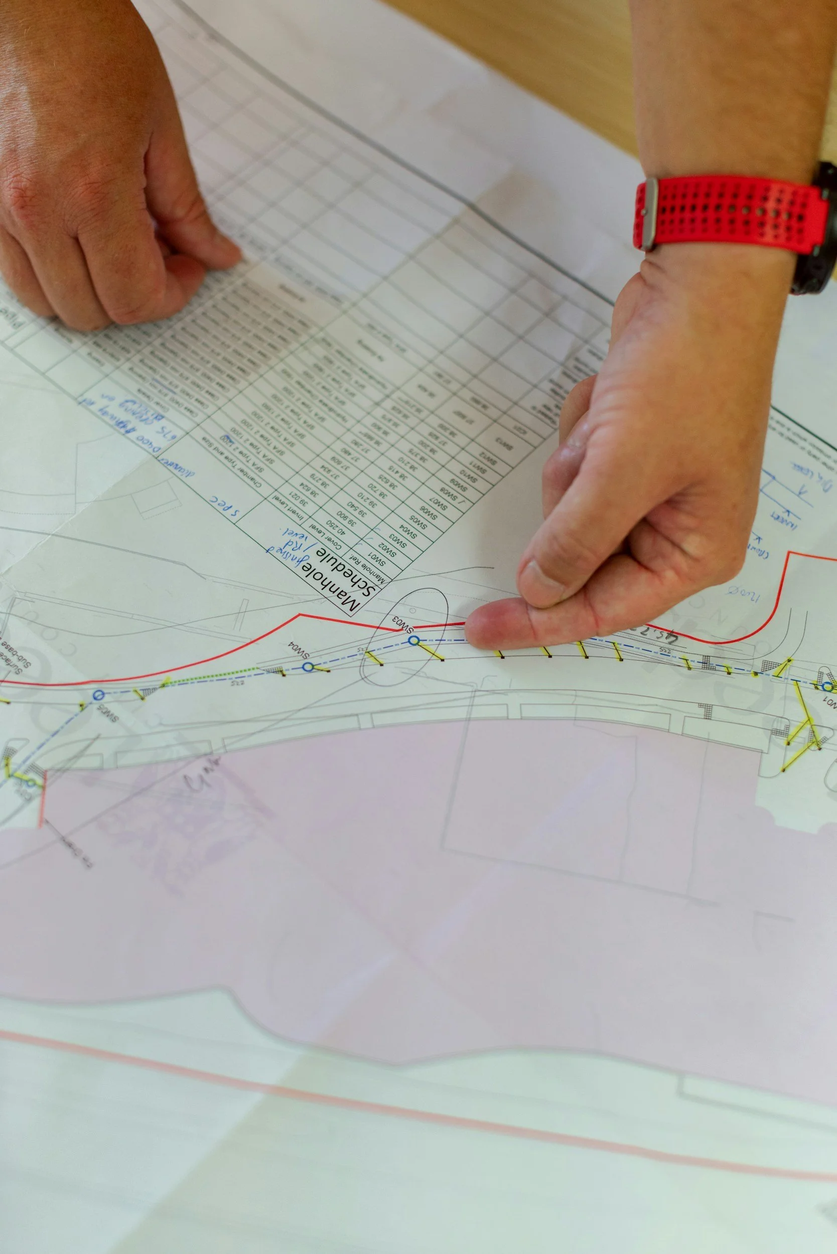 Close-up of hands pointing at a printed map or blueprint with detailed plans, labels, and colored lines.