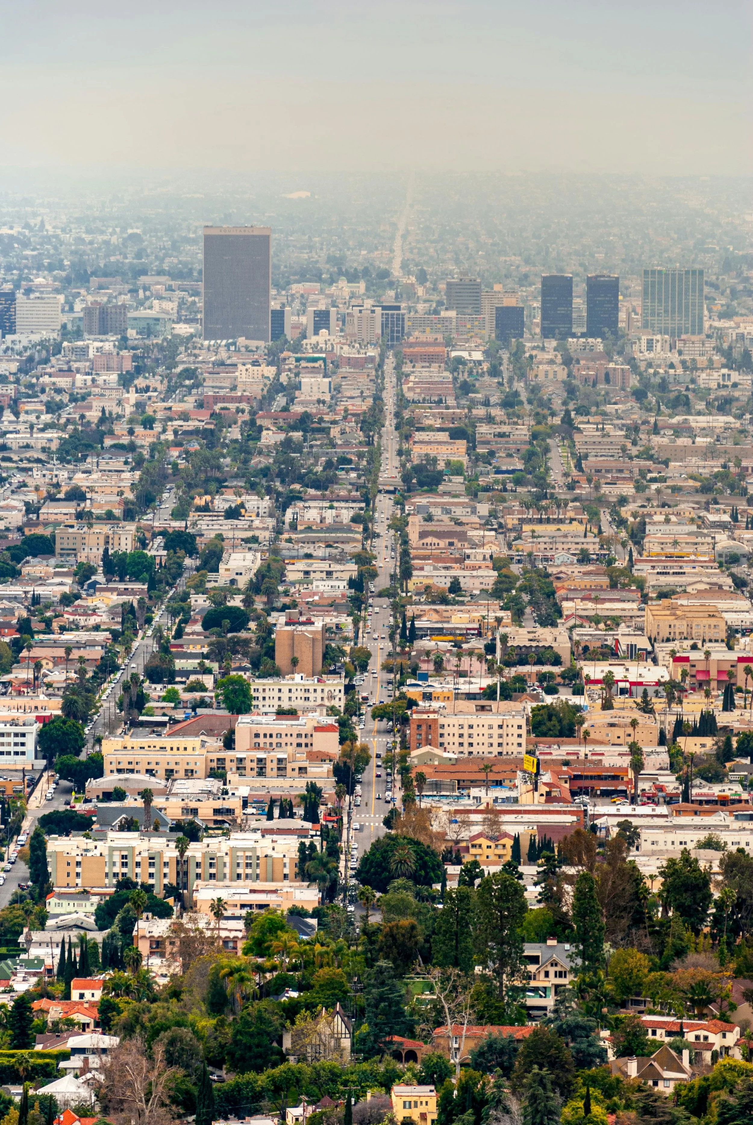 A cityscape with numerous buildings, amidst streets with cars, with a hazy sky in the background.