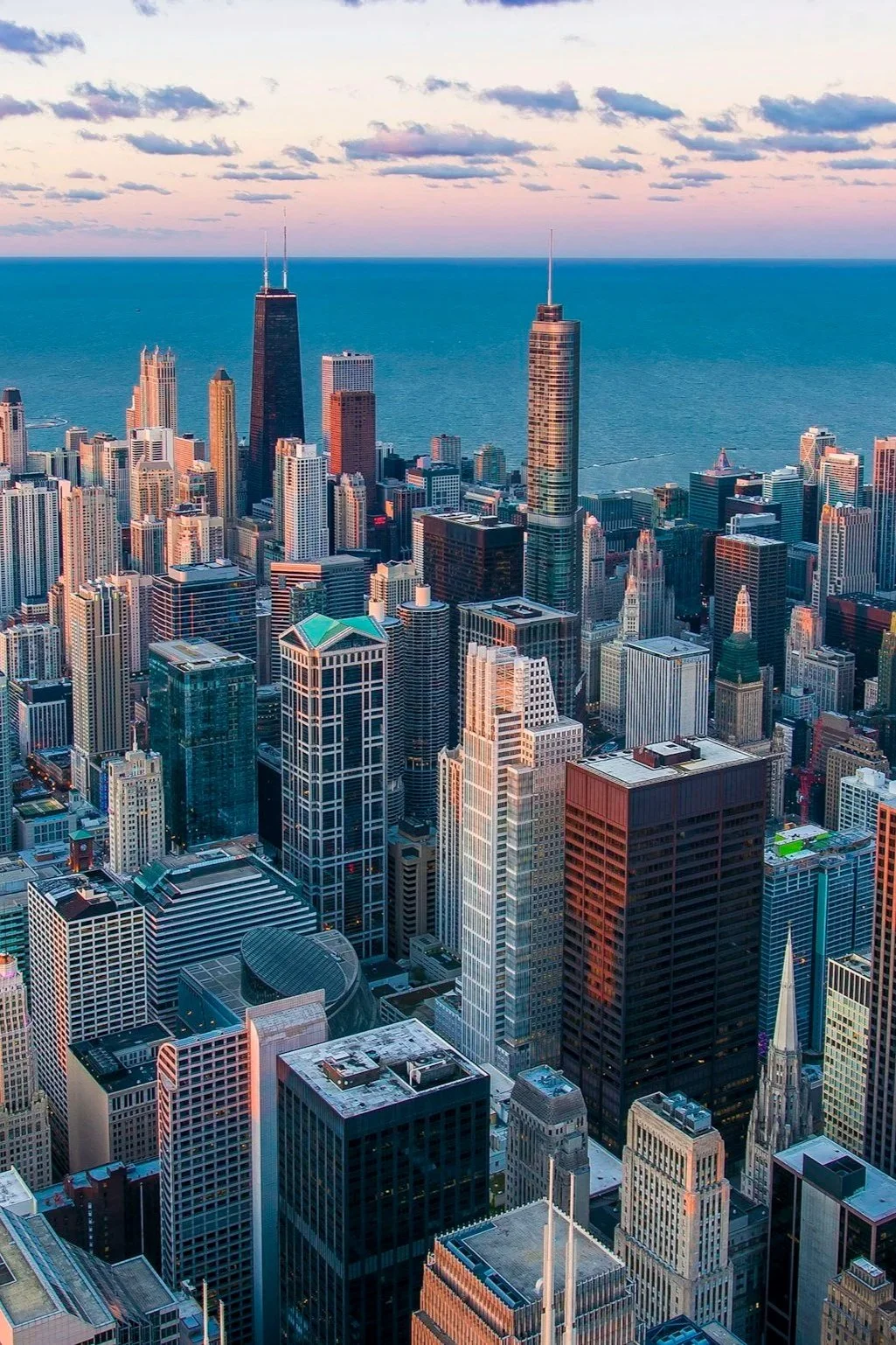 Aerial view of downtown Chicago at sunset with numerous skyscrapers, including the John Hancock Center near Lake Michigan.