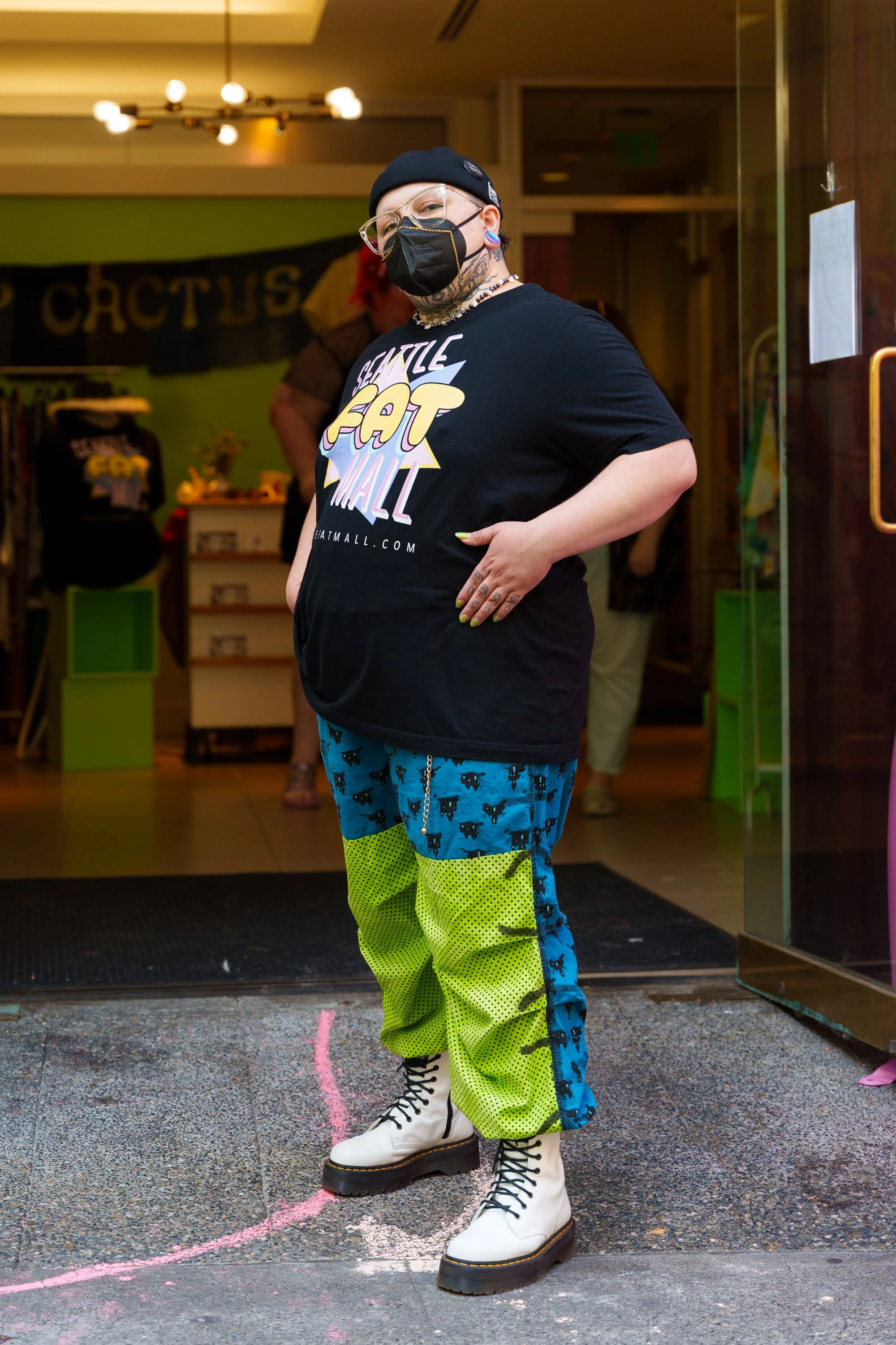 A photo of the founder in a K95 mask with a gold mask chain, a Seattle Fat Mall oversize Tshirt with Blue and Green baggy pants with a gold chain hanging from belt loops. Complete with a brimless hat and platform white doc marten boots.